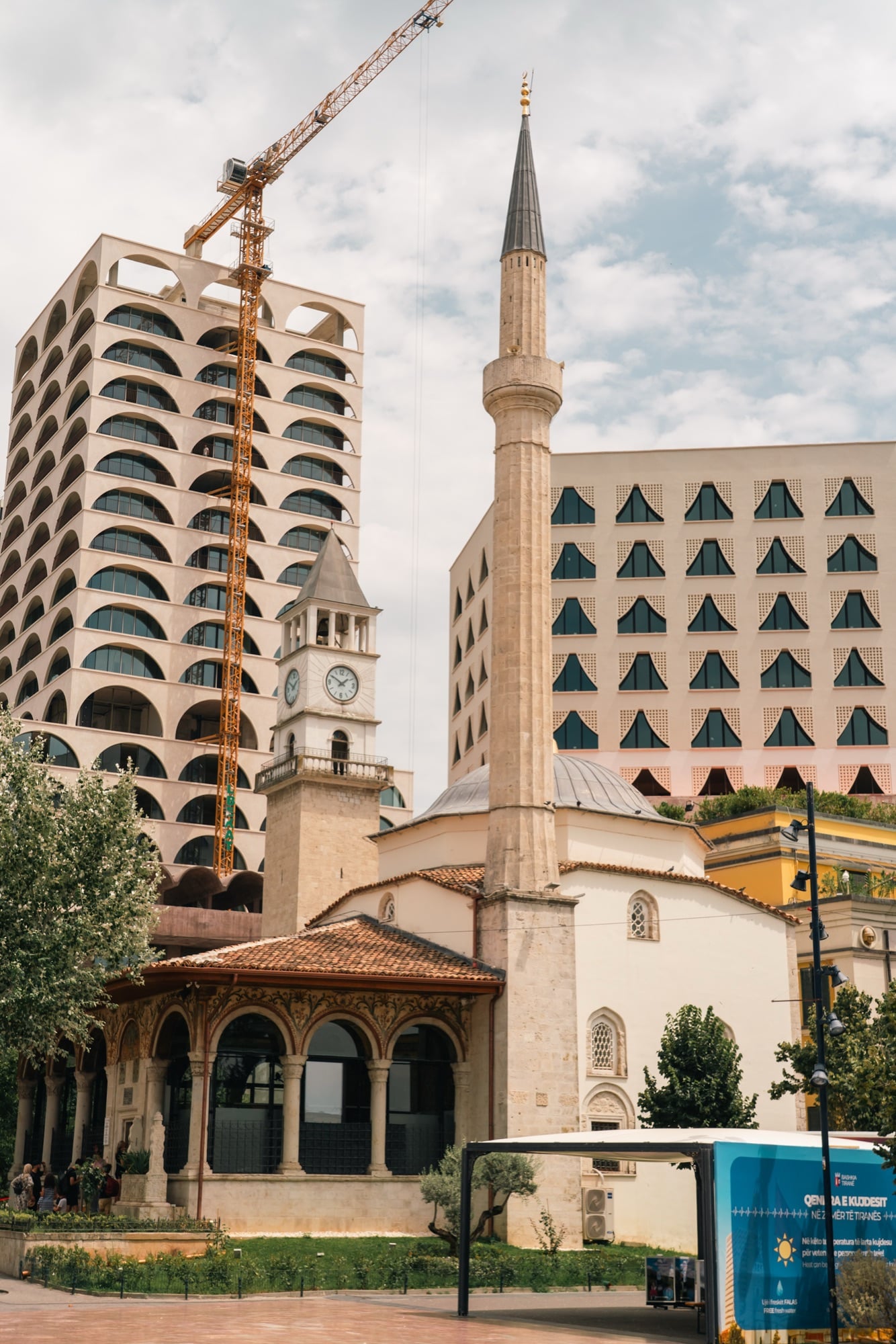 The Et'hem Bey Mosque and its tall minaret beside the Clock Tower of Tirana, an arched modern tower and crane behind