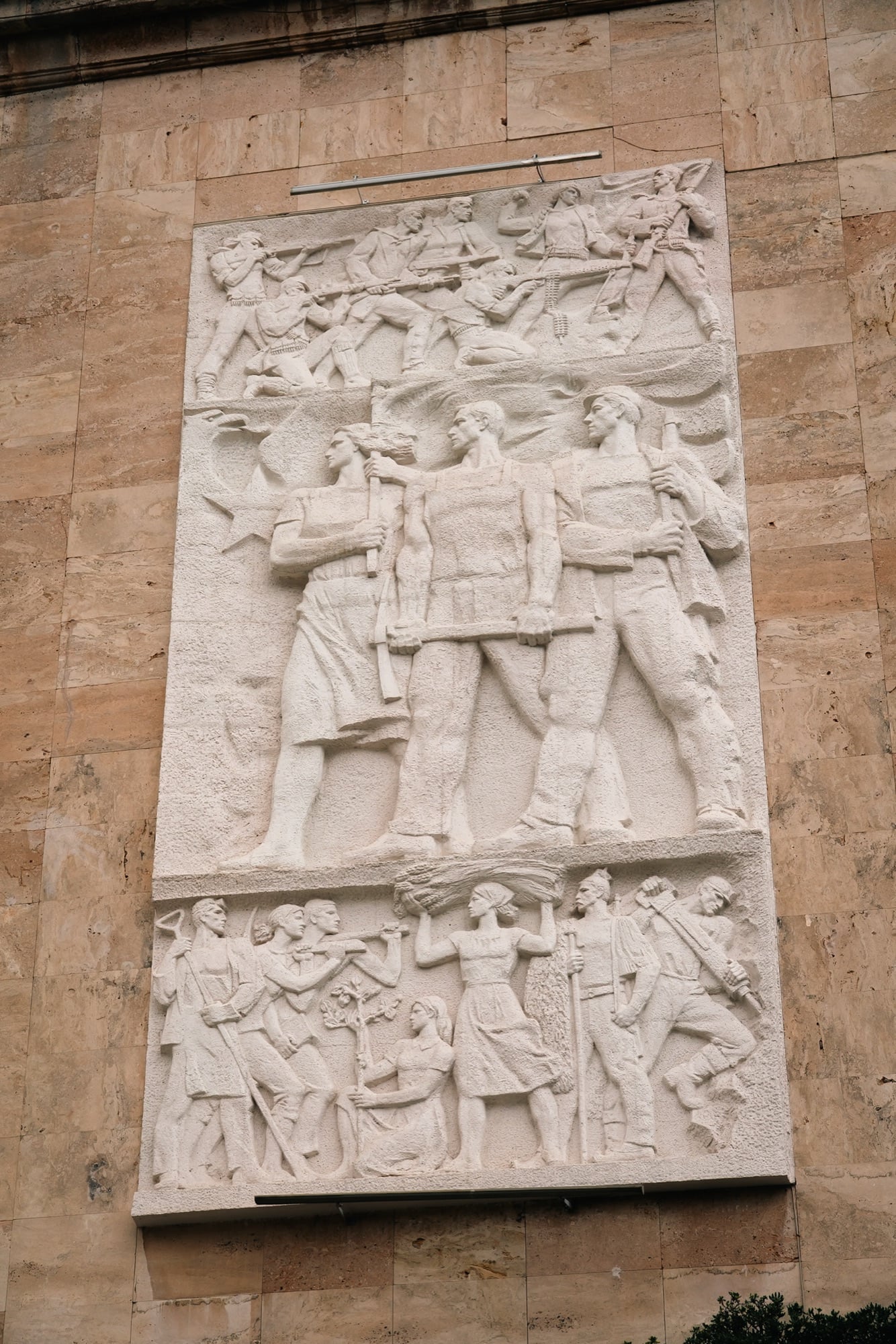 A socialist-realist stone relief of partisans and workers mounted on a travertine facade in Tirana