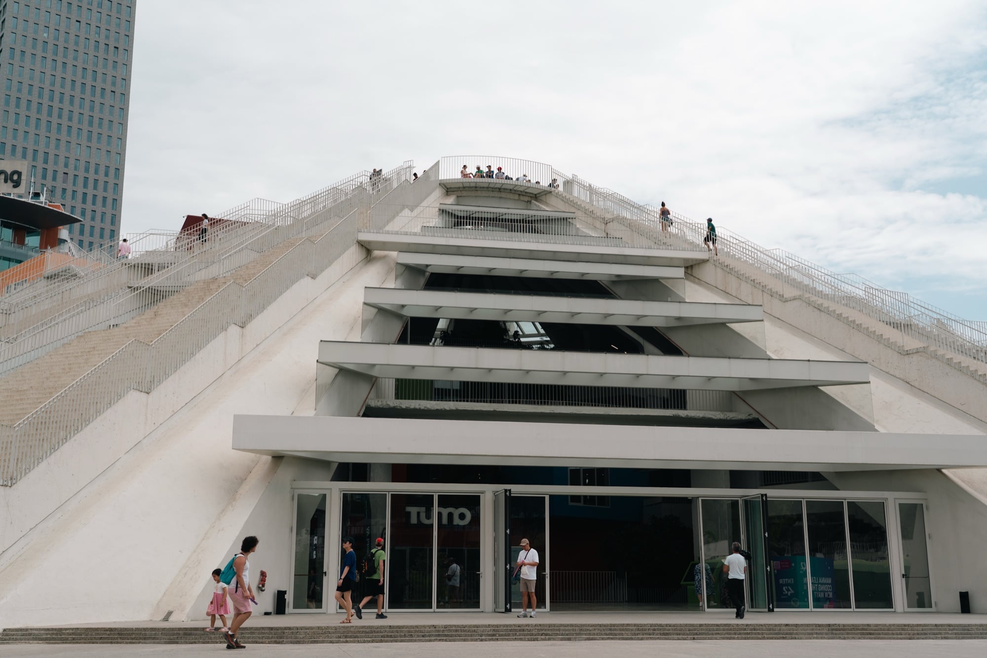 Visitors climbing the white stepped slopes of the Pyramid of Tirana, its terraced ramps and stairs against the sky