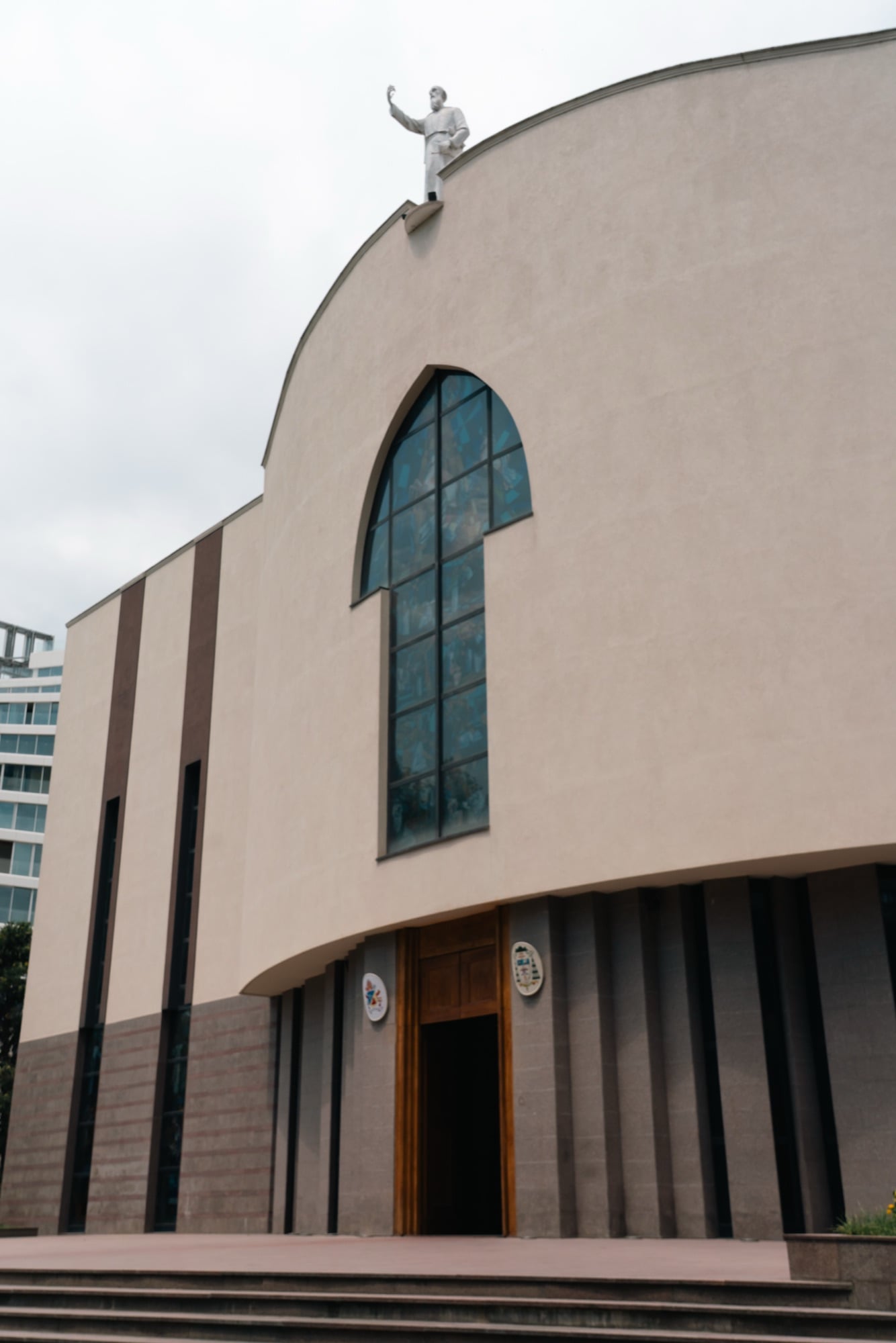 The curved beige facade of St Paul's Catholic Cathedral with its tall arched stained-glass window and rooftop statue
