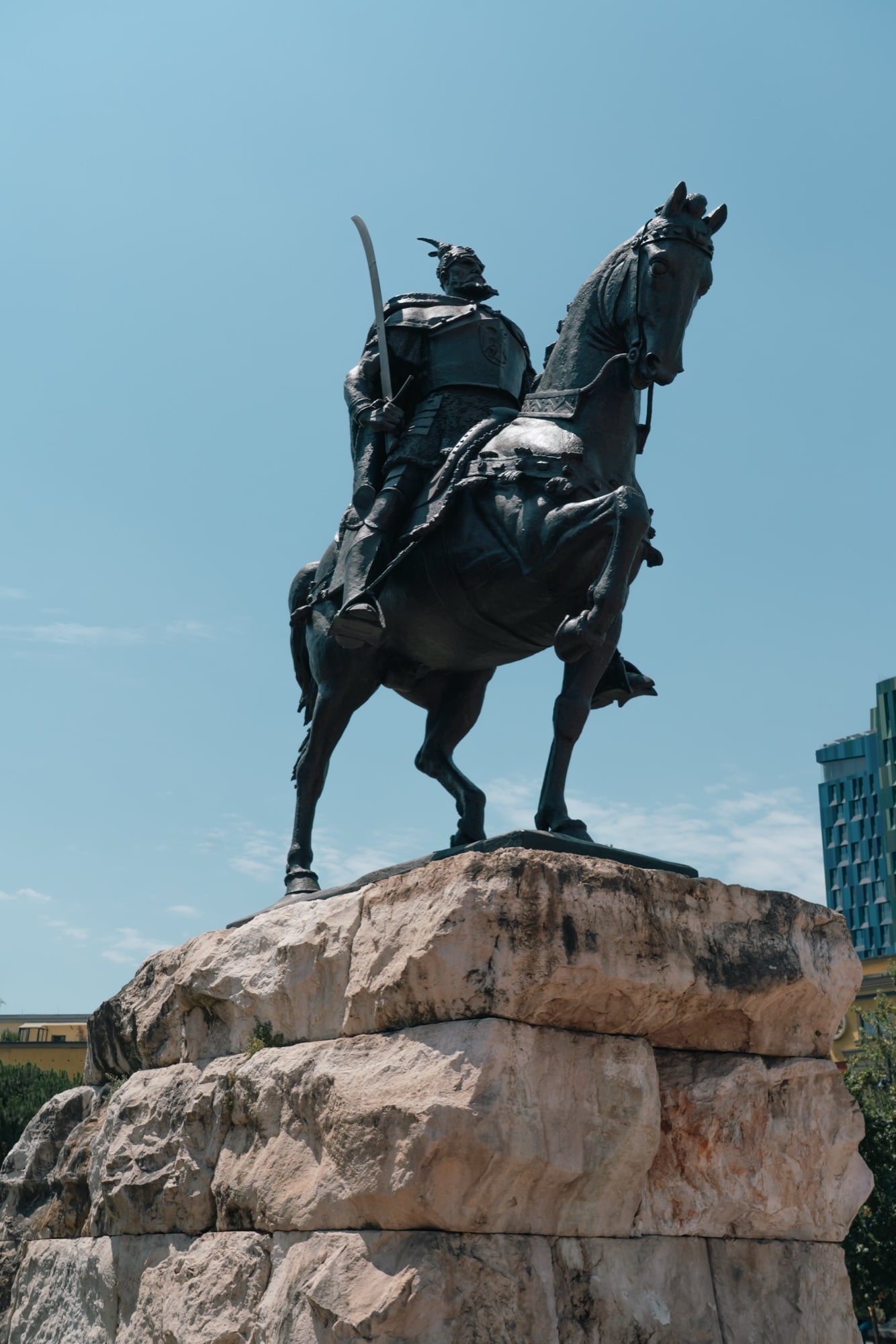 The Skanderbeg equestrian statue rearing against a bright blue sky above its rough stone plinth
