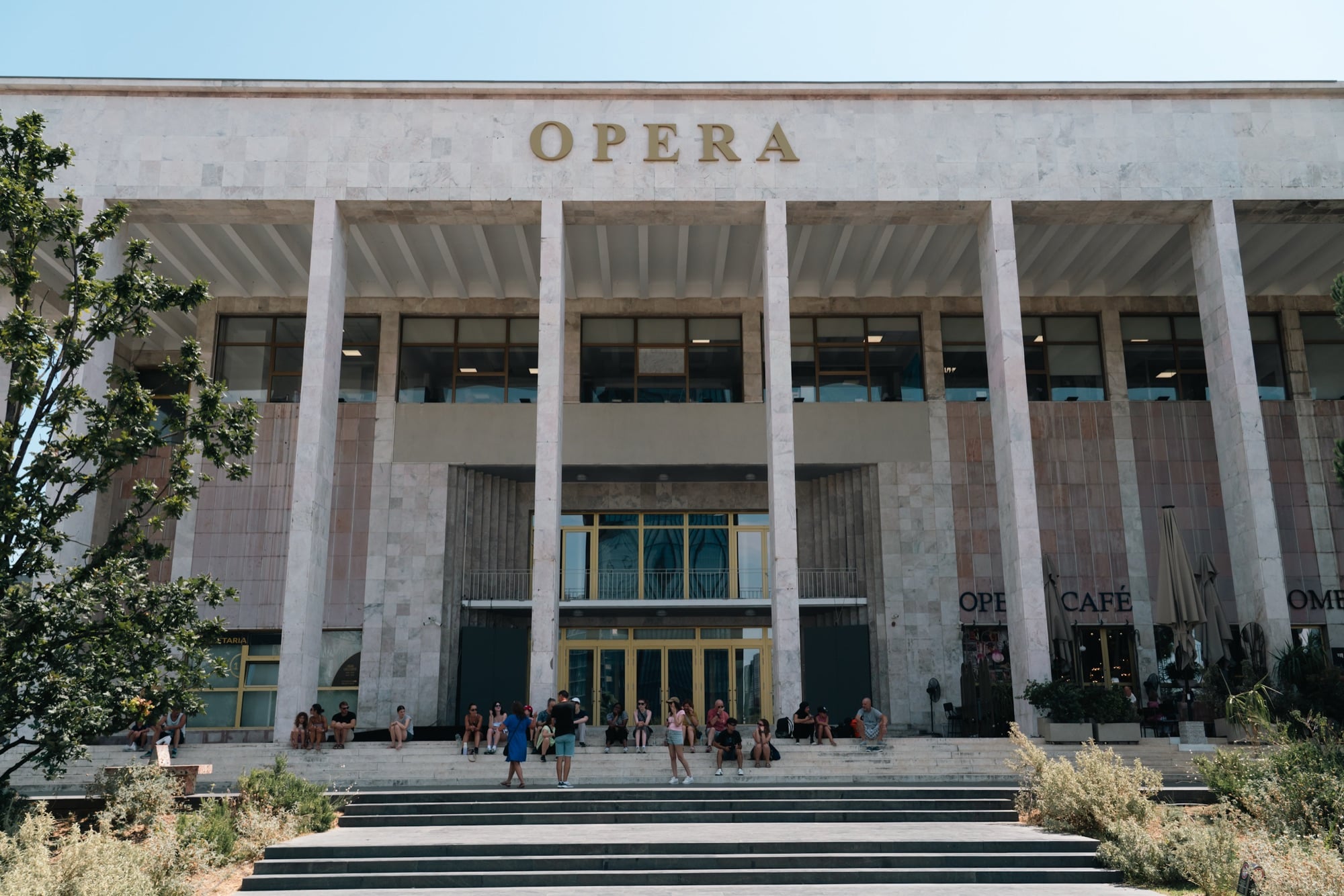 The columned marble facade of the National Theatre of Opera and Ballet, visitors resting on the steps below the OPERA lettering