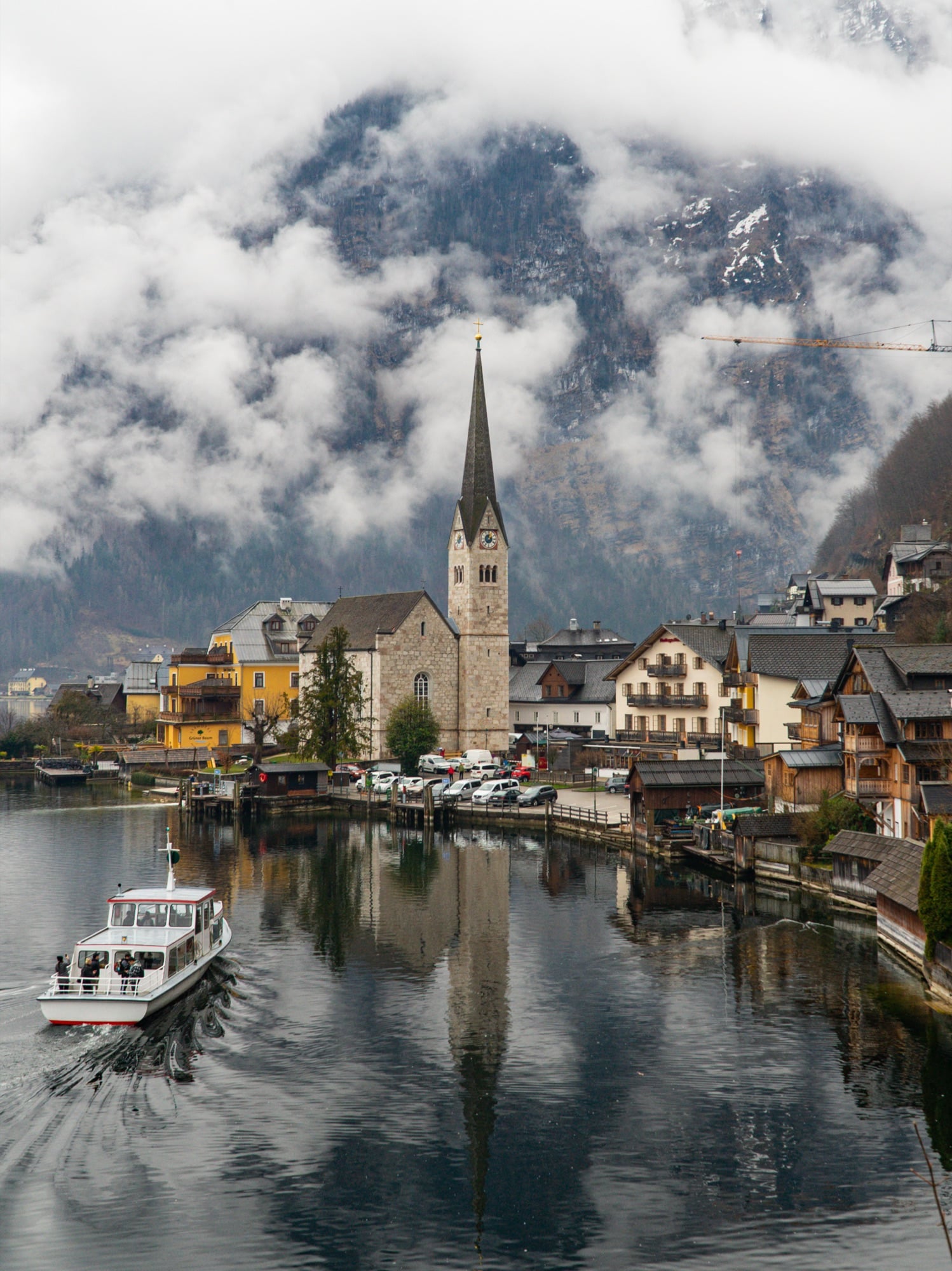 A boat crossing the lake before the reflected church and pastel houses, Hallstatt