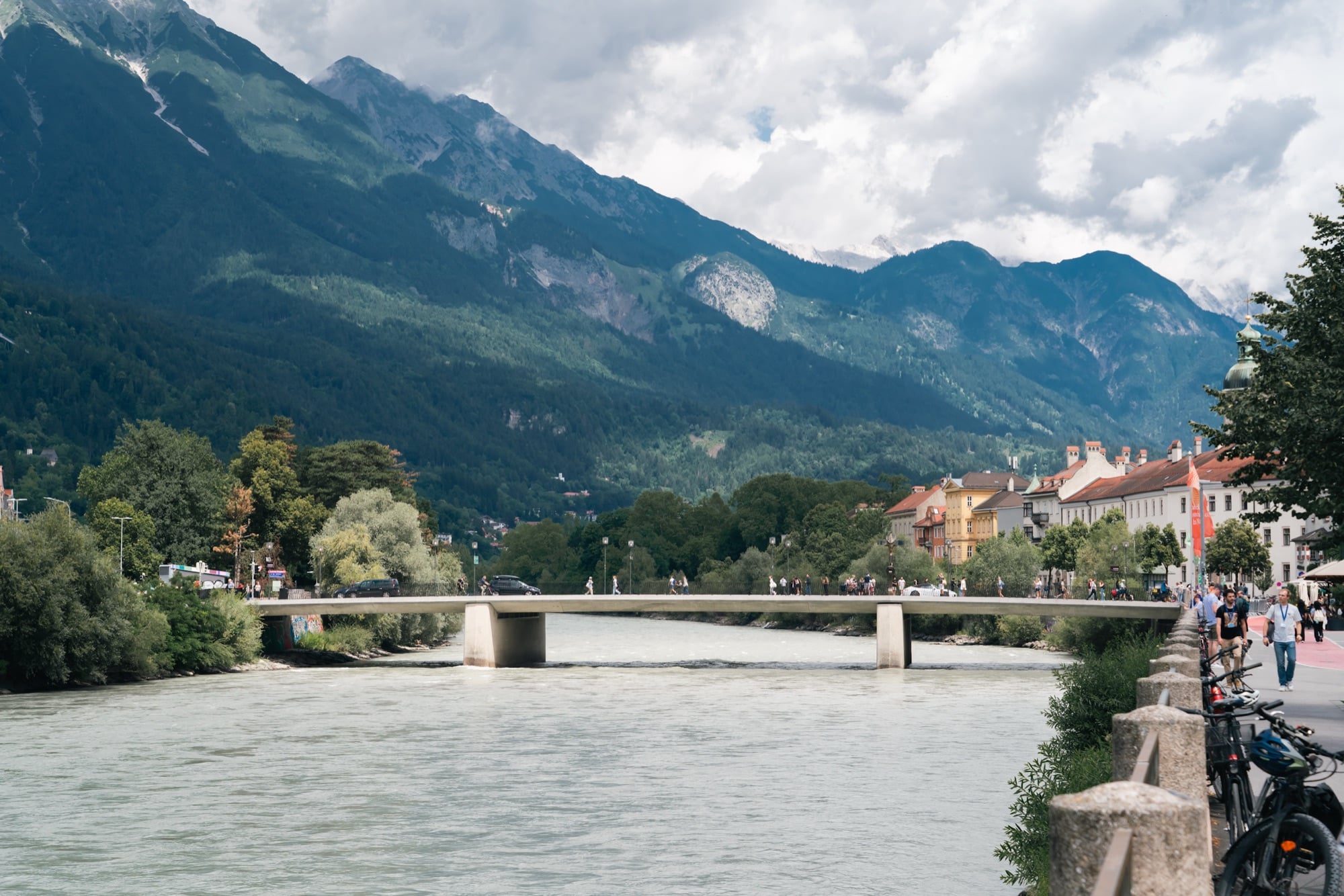 A bridge over the fast green Inn with riverfront houses and mountains beyond, Innsbruck