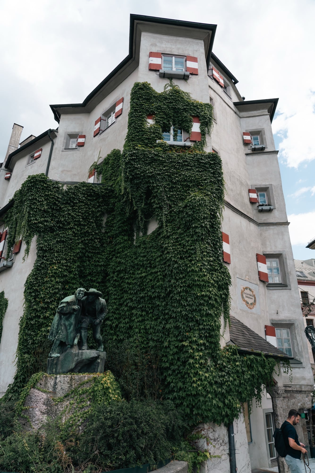 An ivy-clad building above a bronze monument, Innsbruck