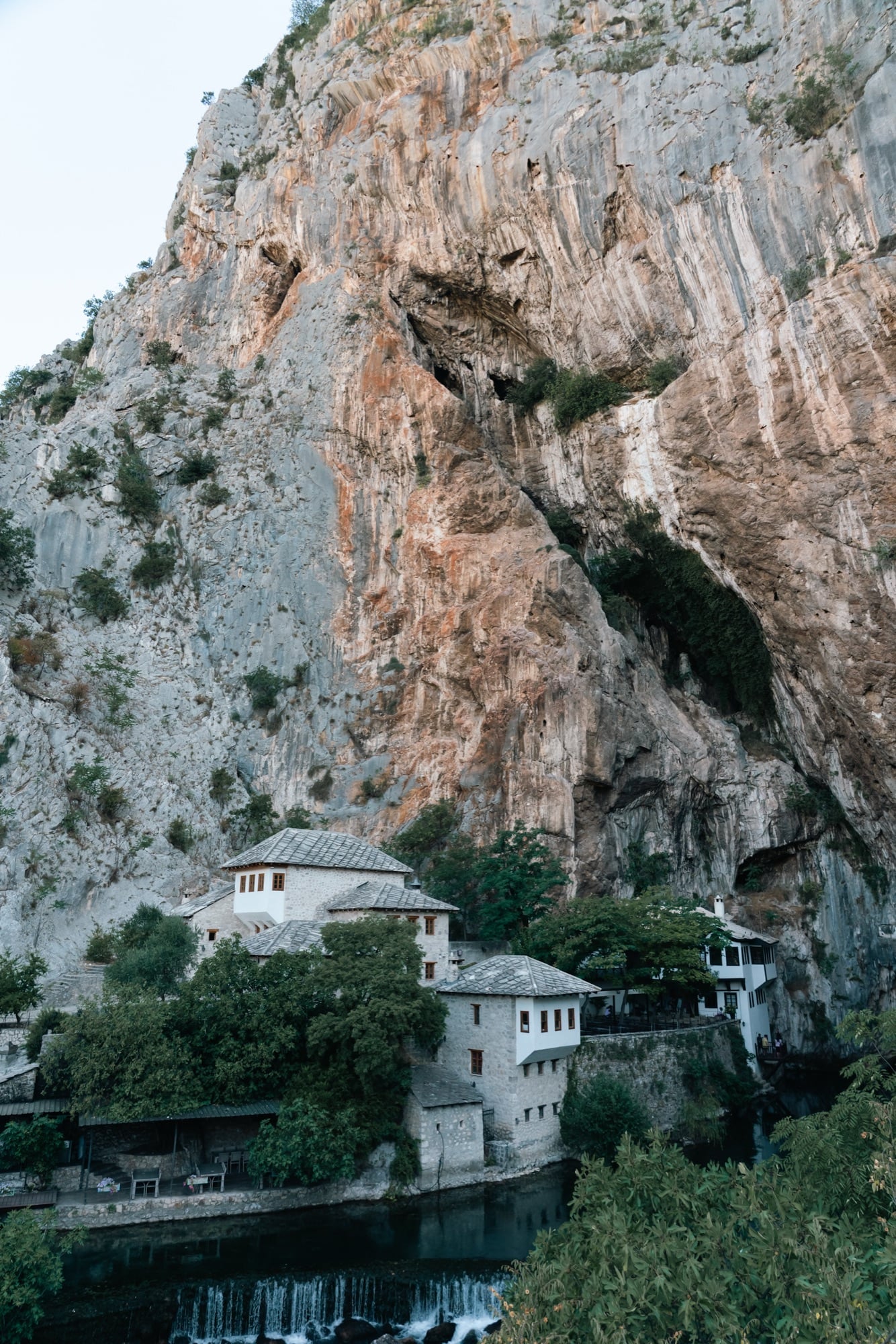 The white Blagaj Tekija, a Sufi dervish house, tucked beneath a towering limestone cliff at the source of the Buna river, water spilling over rocks below