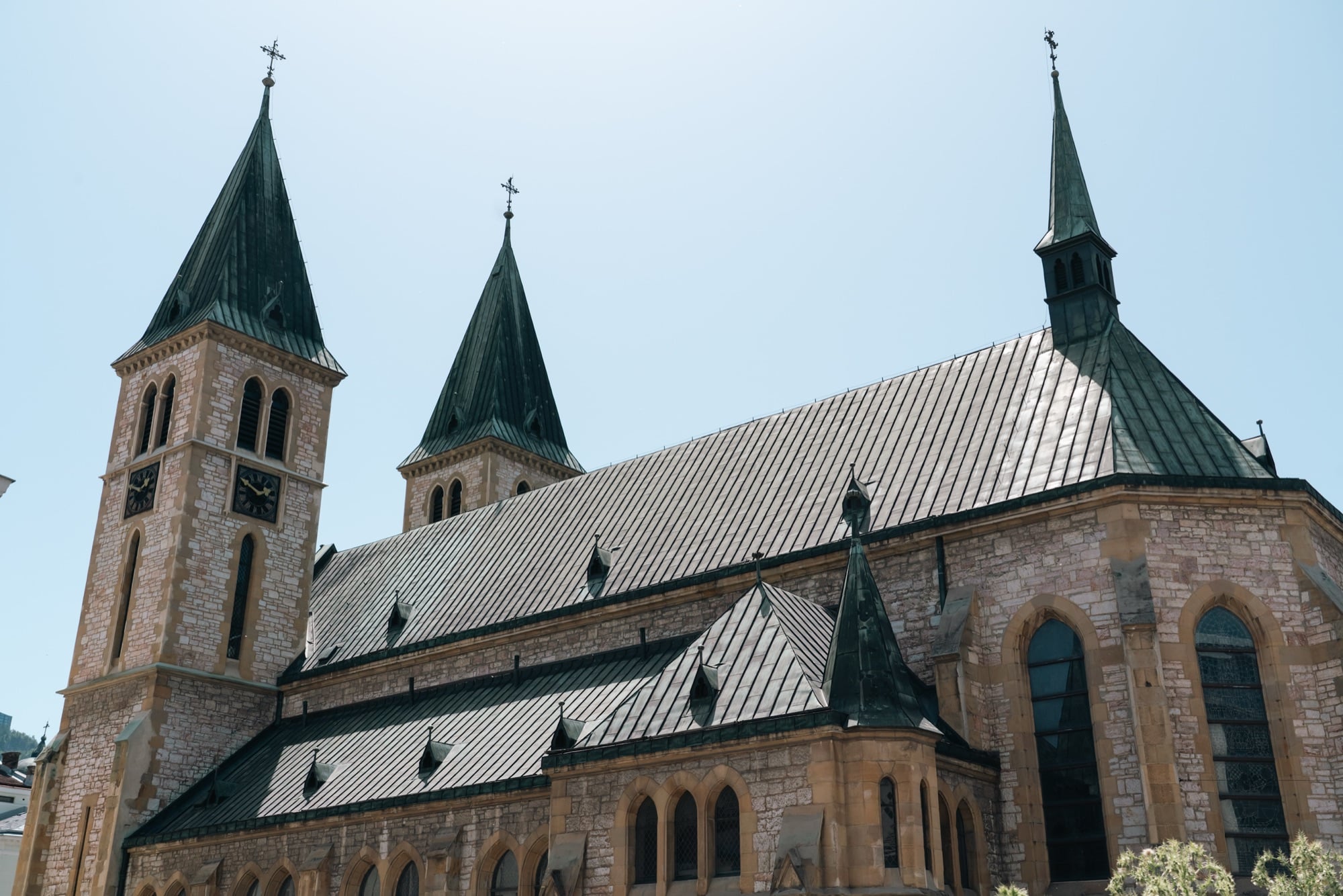 The green Gothic spires and steep metal roof of Sarajevo's Sacred Heart Cathedral rising above its pale stone walls