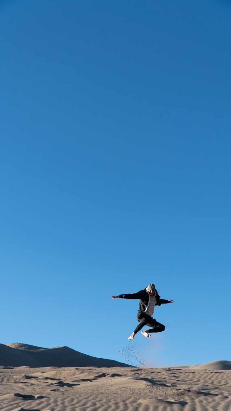 Kendrick leaping mid-air across the sand dunes beneath a clear blue sky