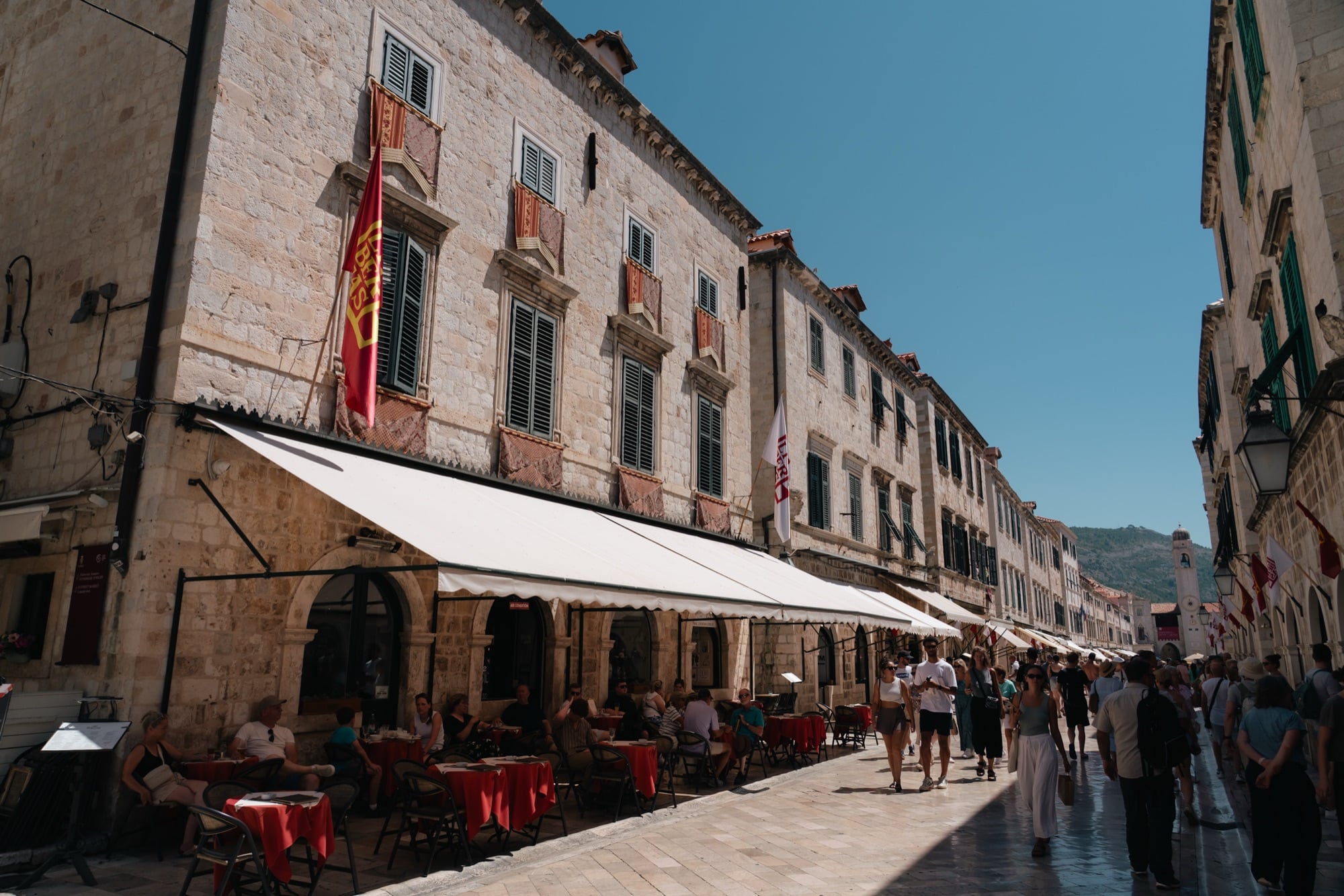 Cafe awnings and red umbrellas along the polished limestone of the Stradun, Dubrovnik