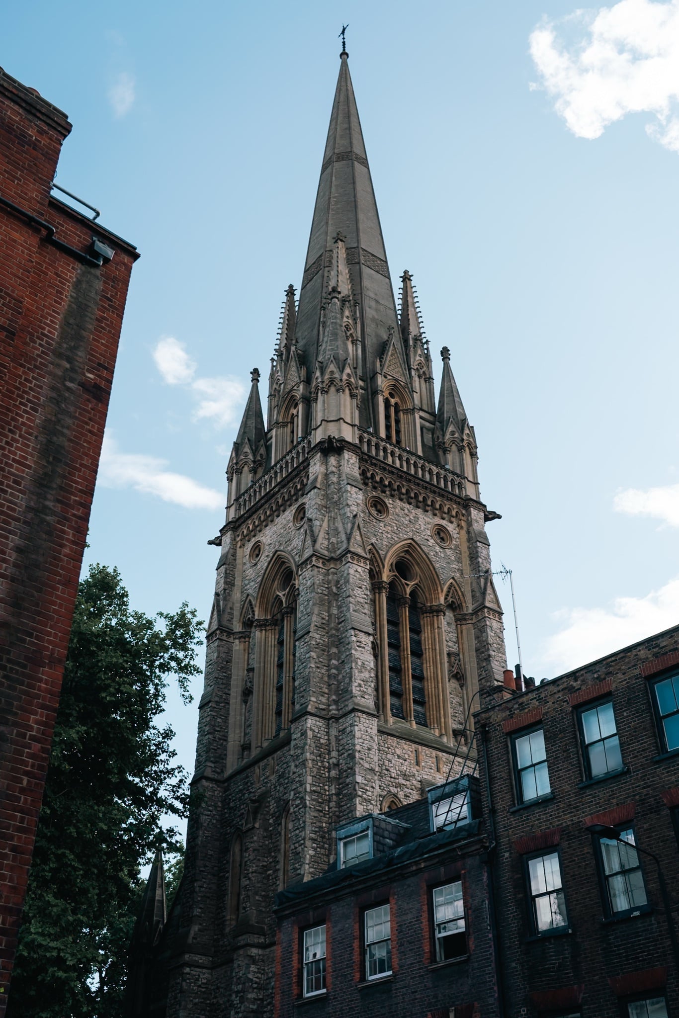 The tall stone spire of a Victorian Gothic church rising between Kensington rooftops