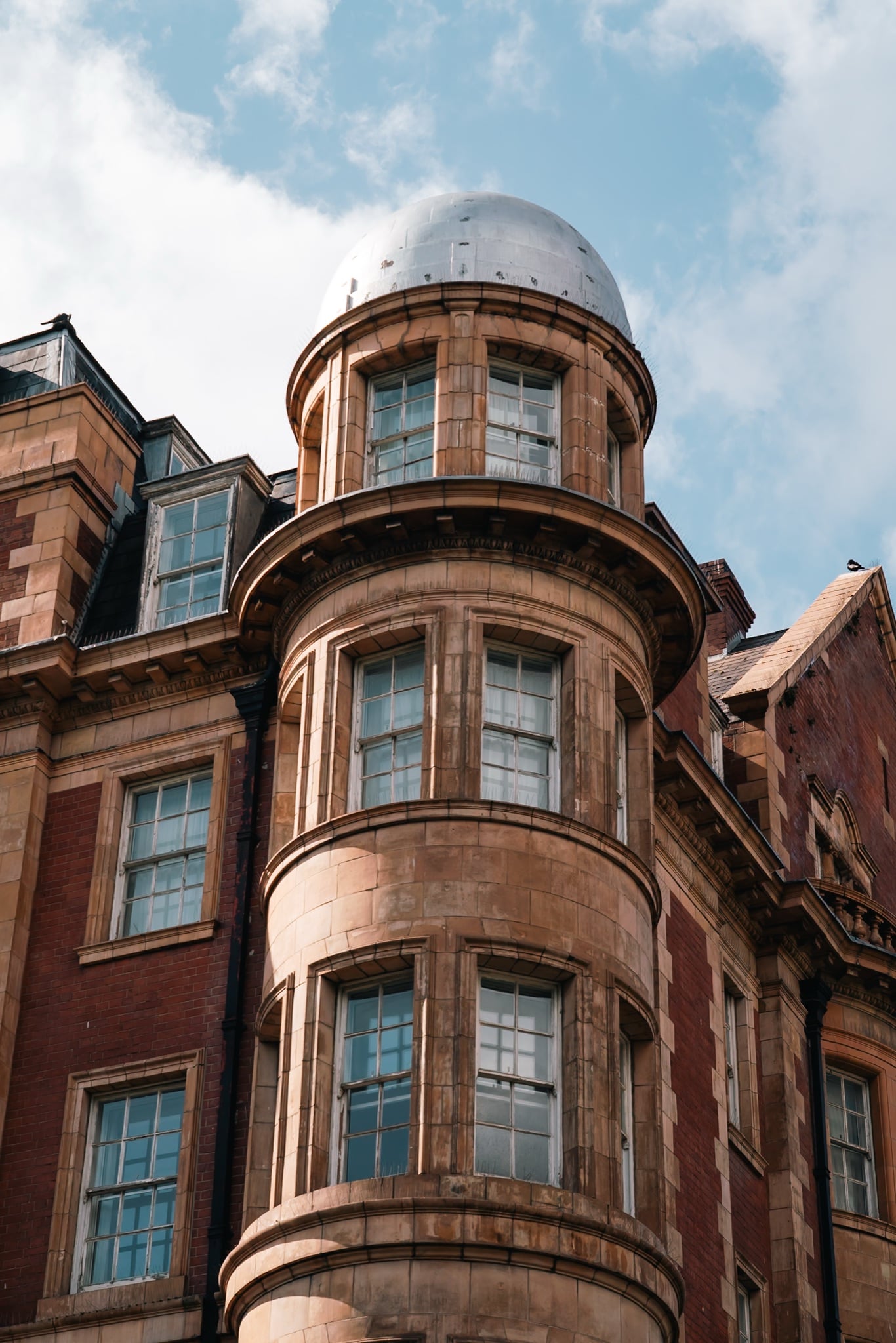A turreted corner building topped by a small silver dome, in brick and sandstone