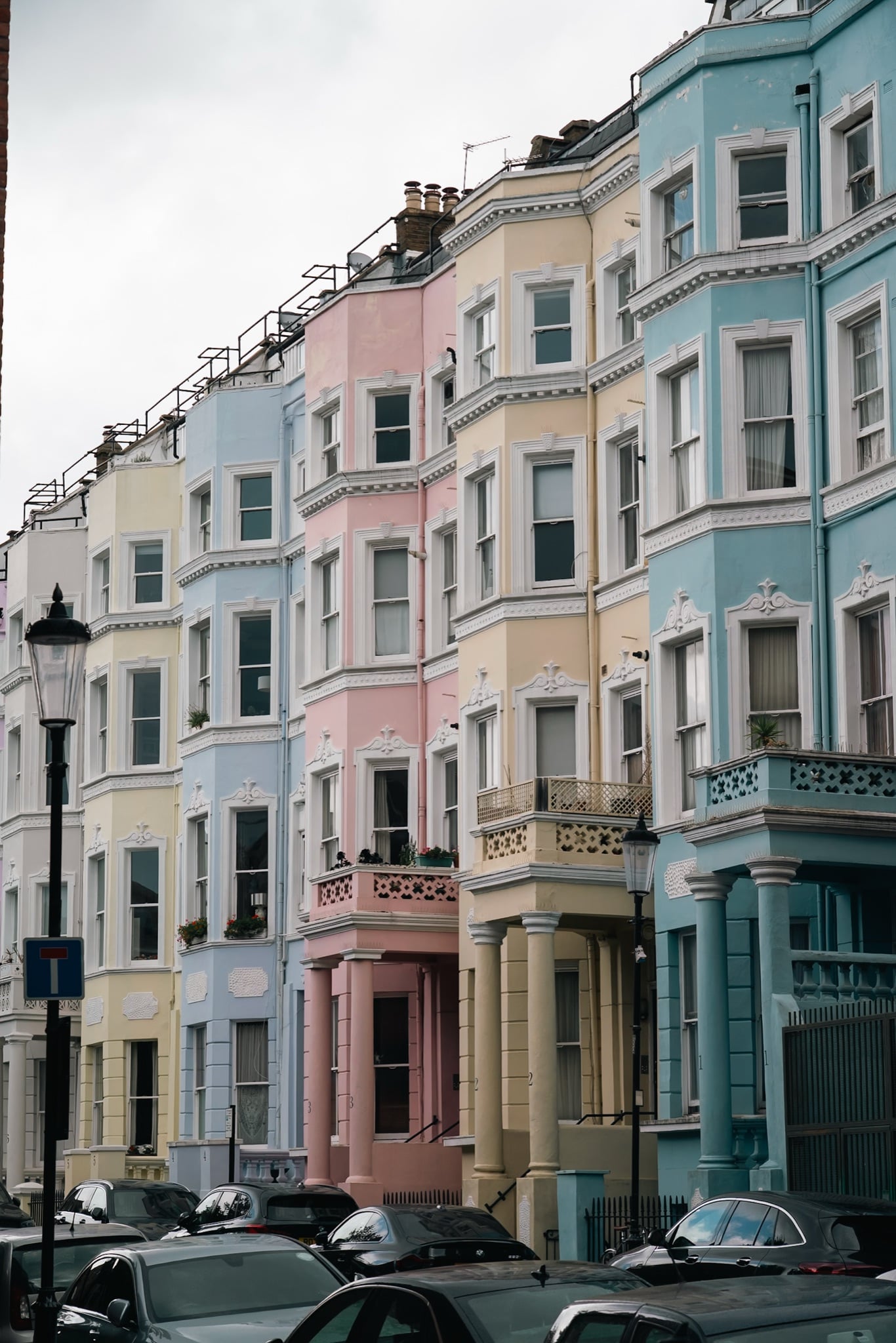 A row of pastel-painted terraced houses above parked cars in Notting Hill