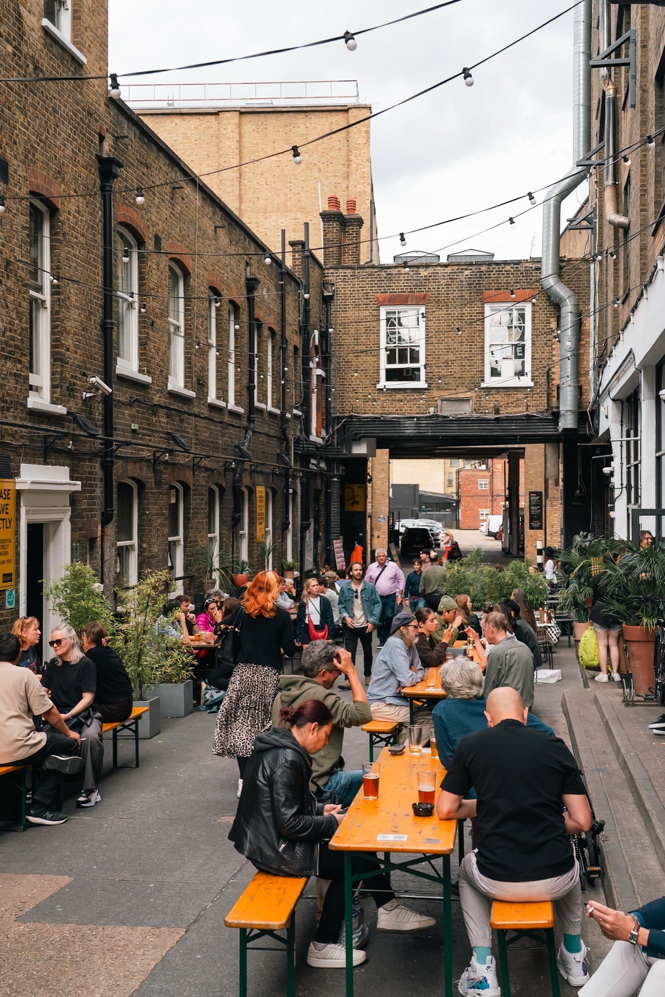 A busy courtyard beer garden strung with festoon lights and lined with communal tables off Brick Lane