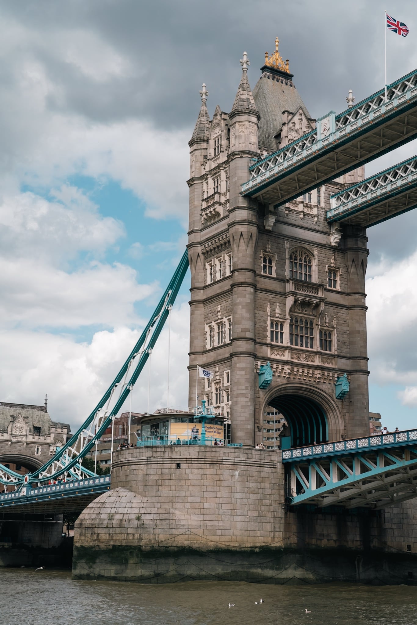 A close view of Tower Bridge's north tower and blue suspension chains from the riverbank