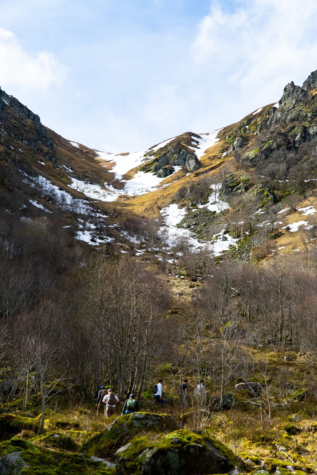 Hikers climbing a snow-streaked valley toward the saddle between rocky Vosges peaks near Gérardmer
