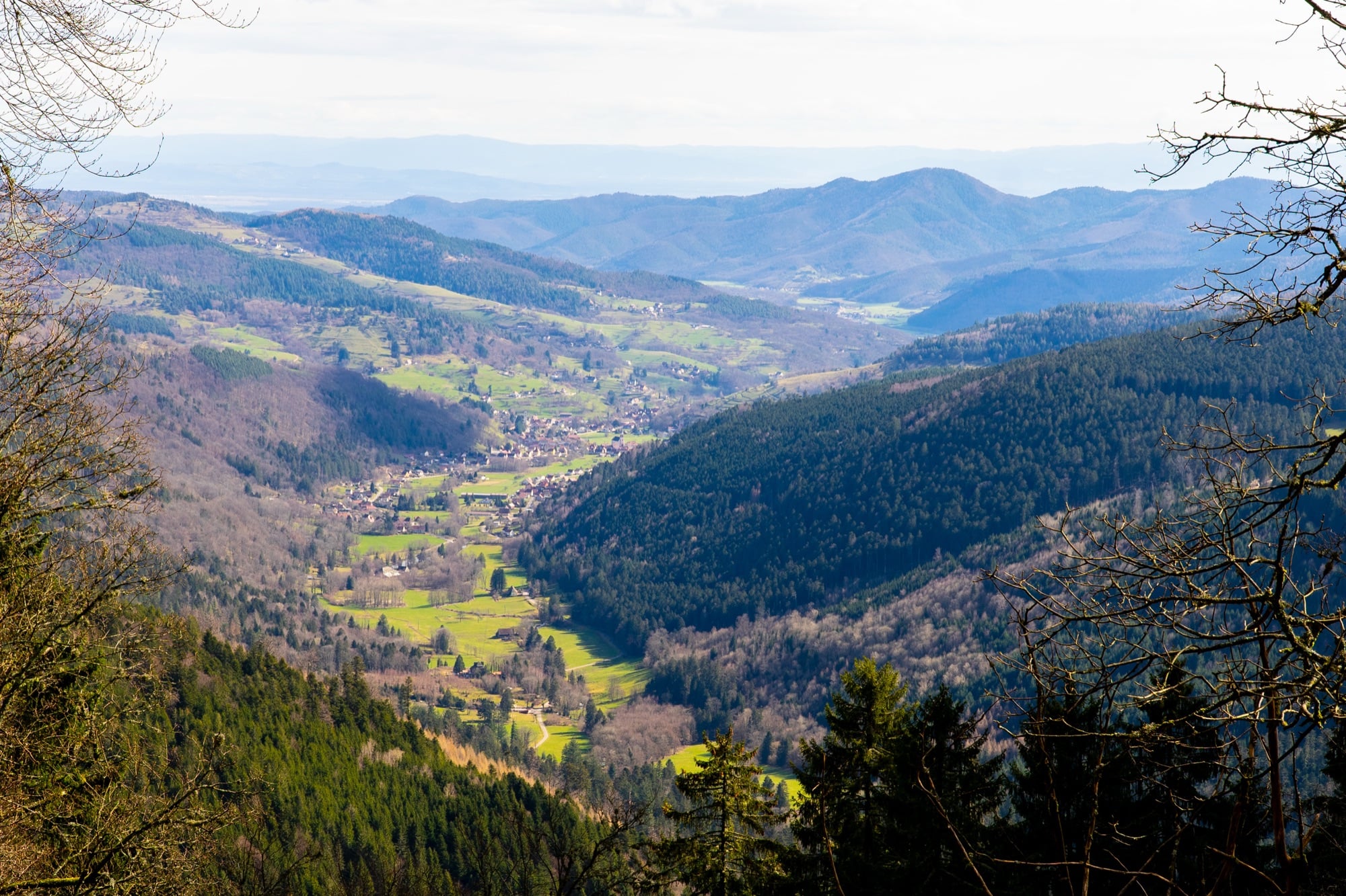 A green Vosges valley with a village nestled below layered, forested ridges near Gérardmer