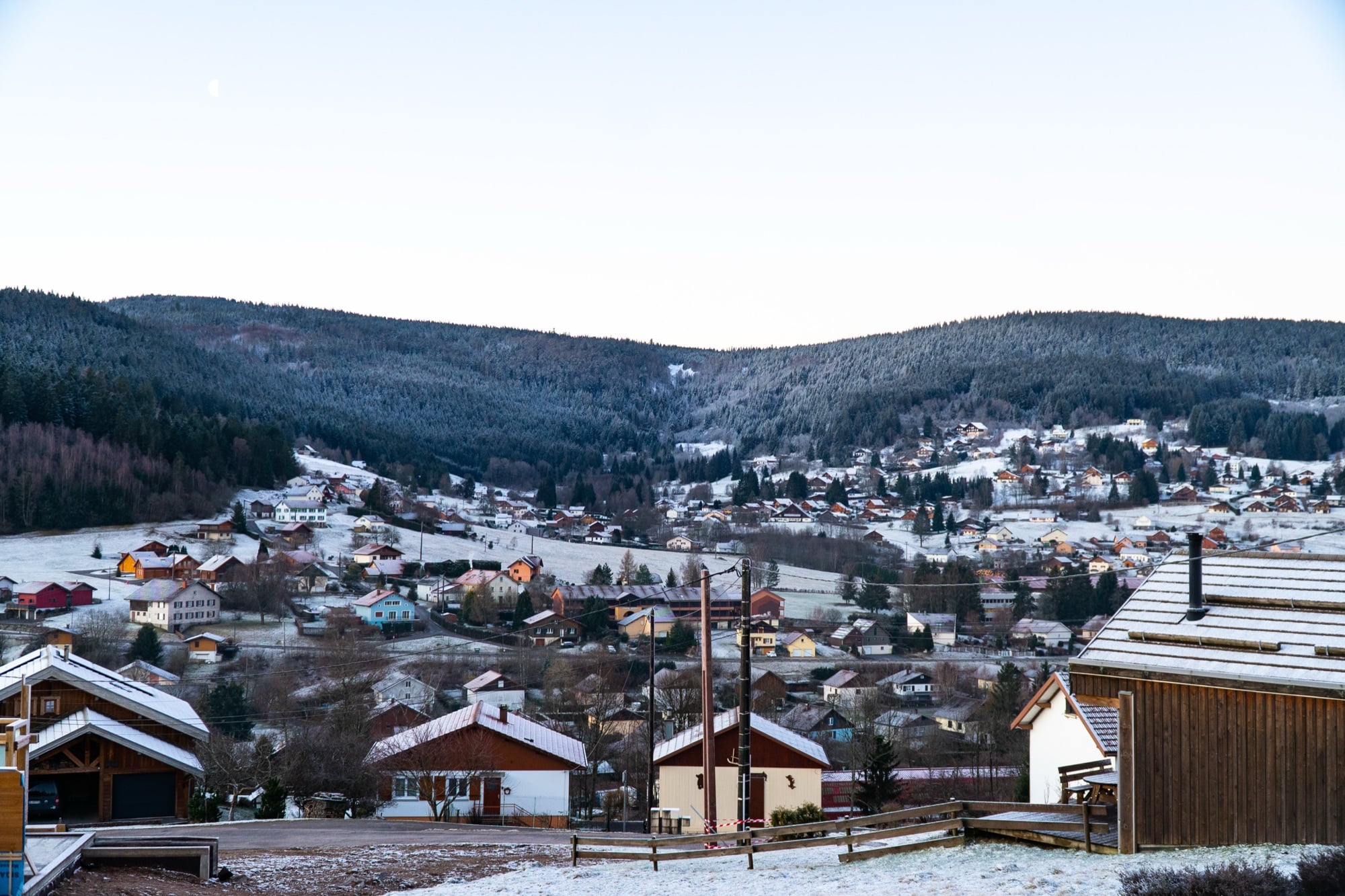 A frost-dusted village at dawn scattered across forested hillsides in the Gérardmer valley