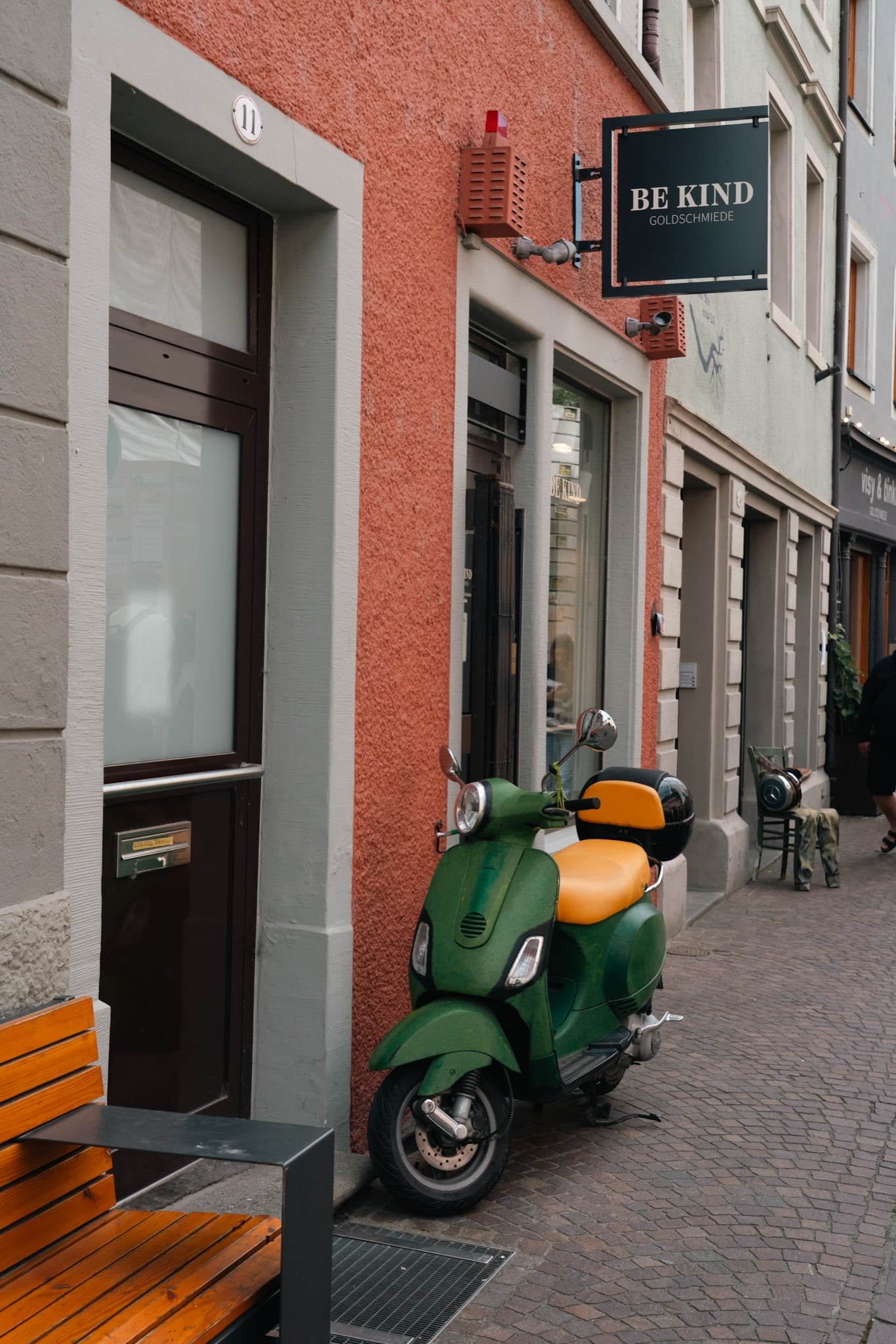 A green vintage scooter parked beneath a goldsmith's sign on a Konstanz side street