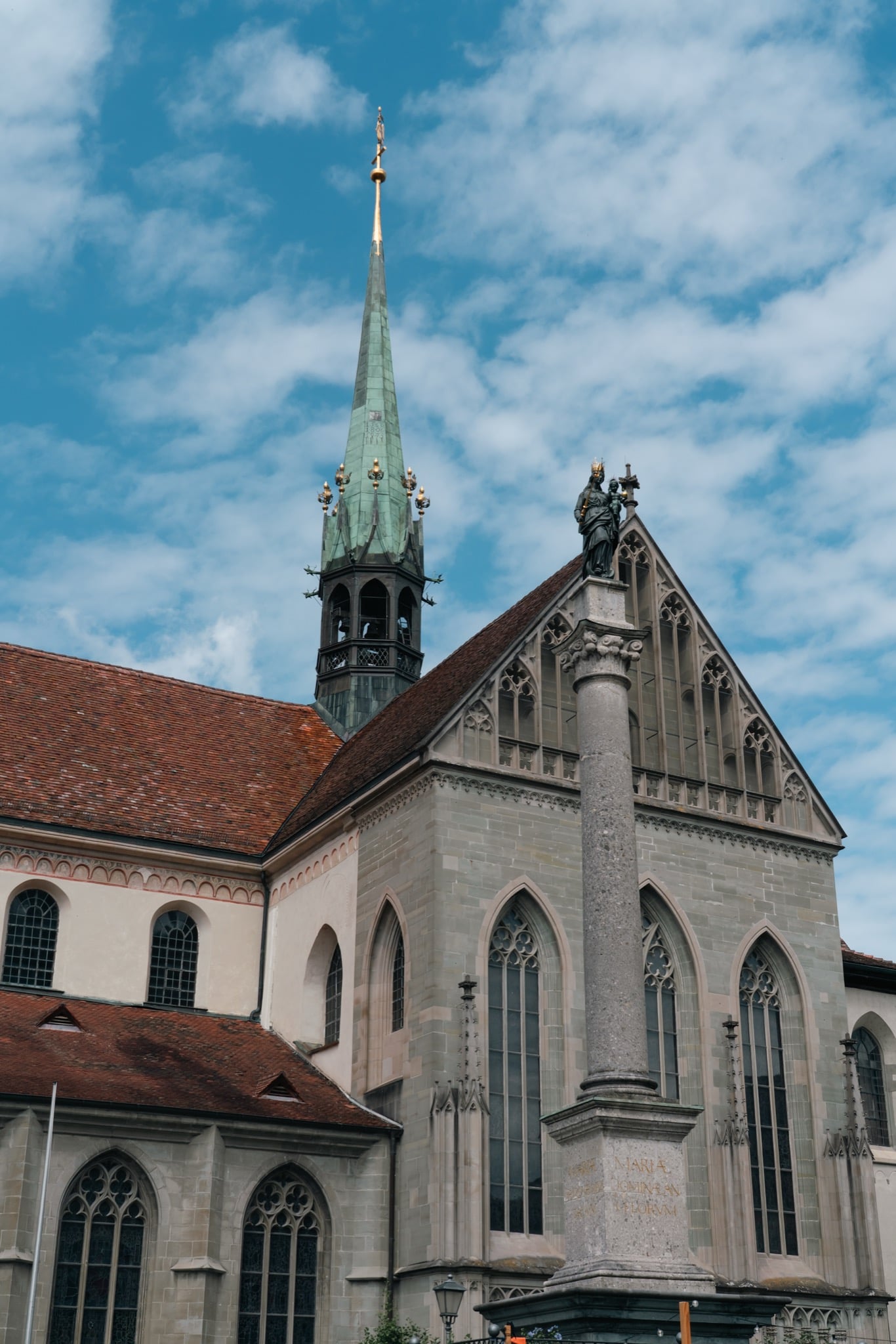 The copper-green spire of the Konstanz Minster above a statue-topped column