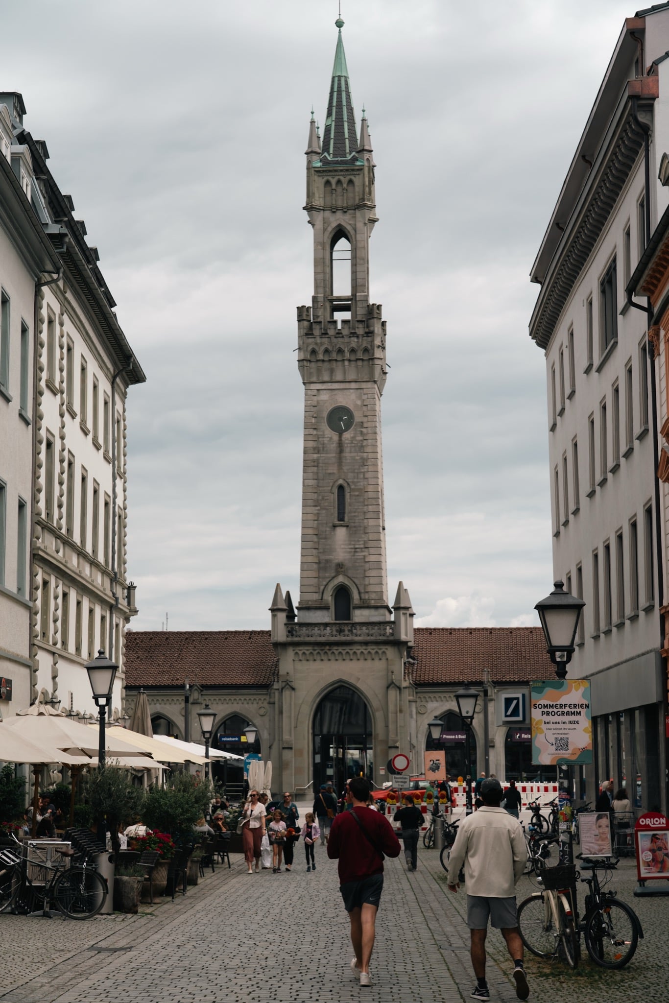 The tall clock tower of Konstanz station seen down a café-lined street