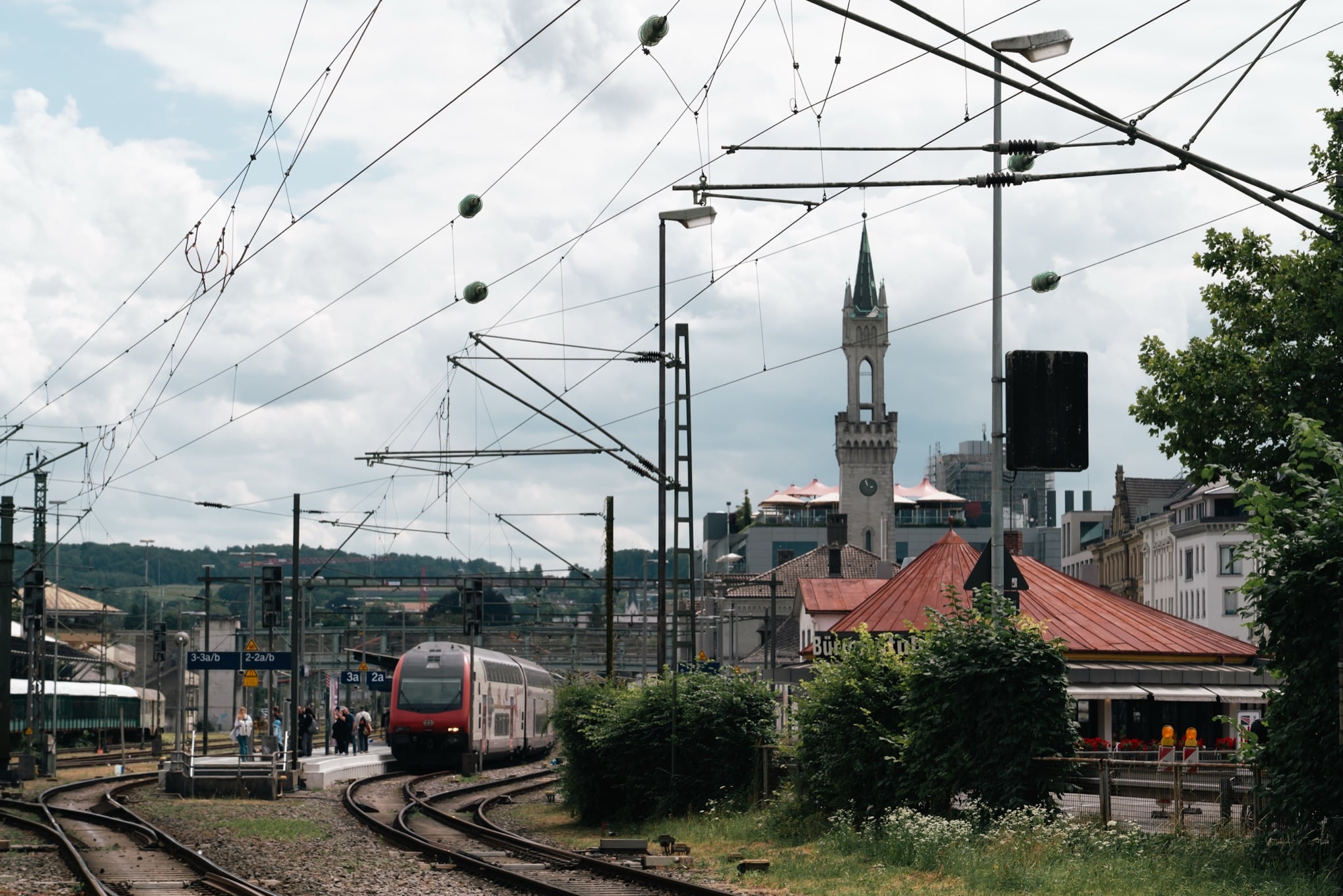 A red double-decker train pulling into Konstanz station, the station tower rising behind