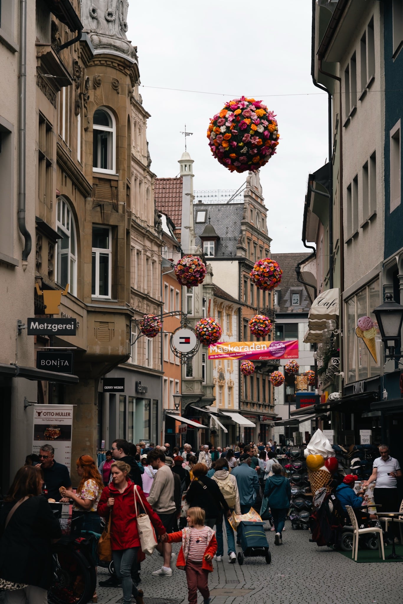 A busy Konstanz shopping street hung with giant flower balls above the crowds