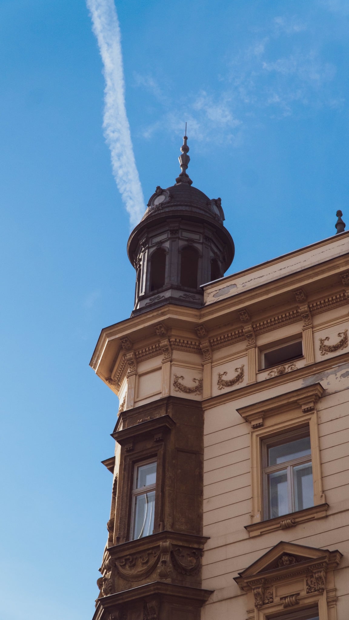 A domed corner cupola reaching into the blue, a jet trail overhead