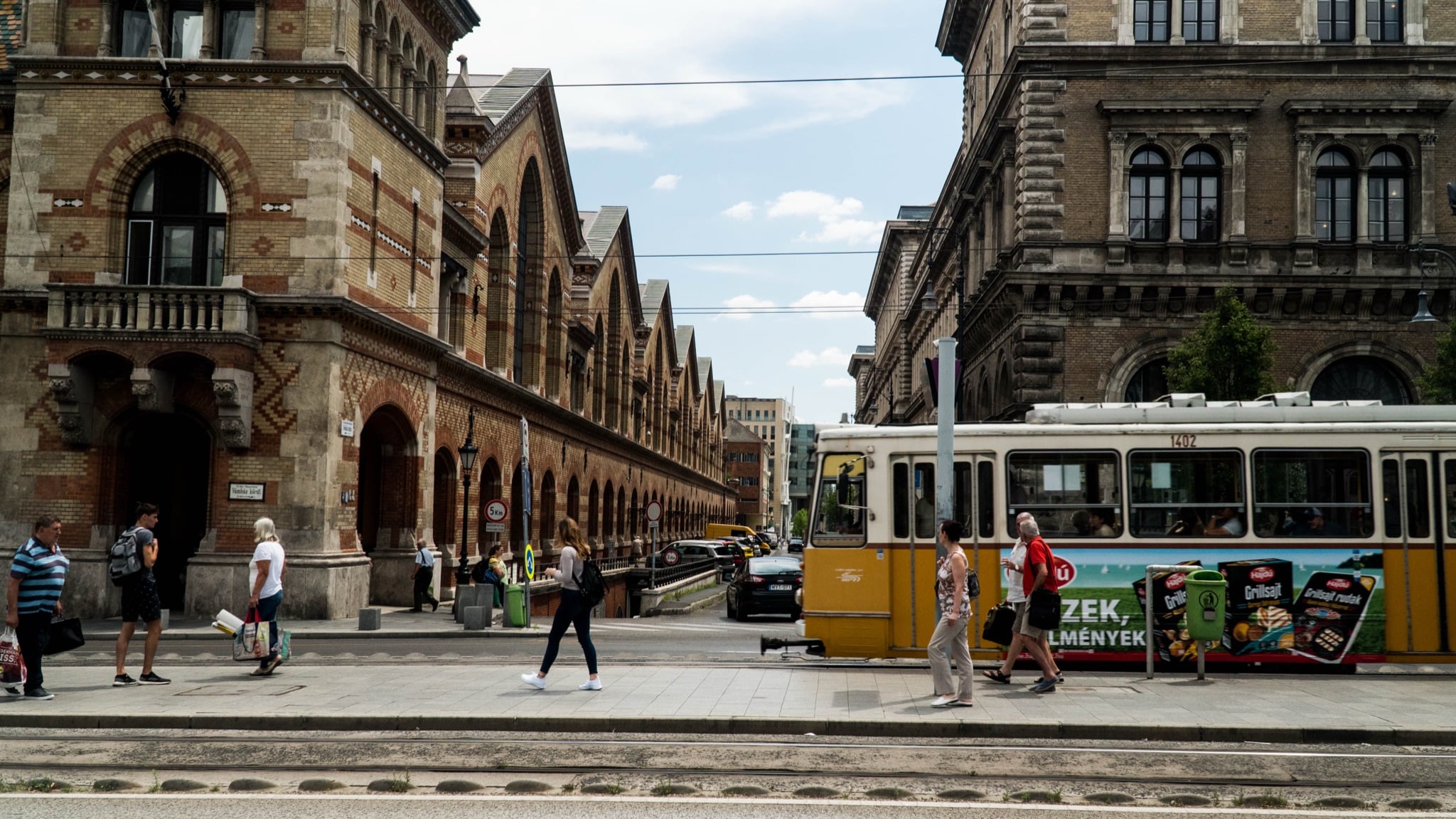A yellow tram passing the arcaded flank of the Great Market Hall
