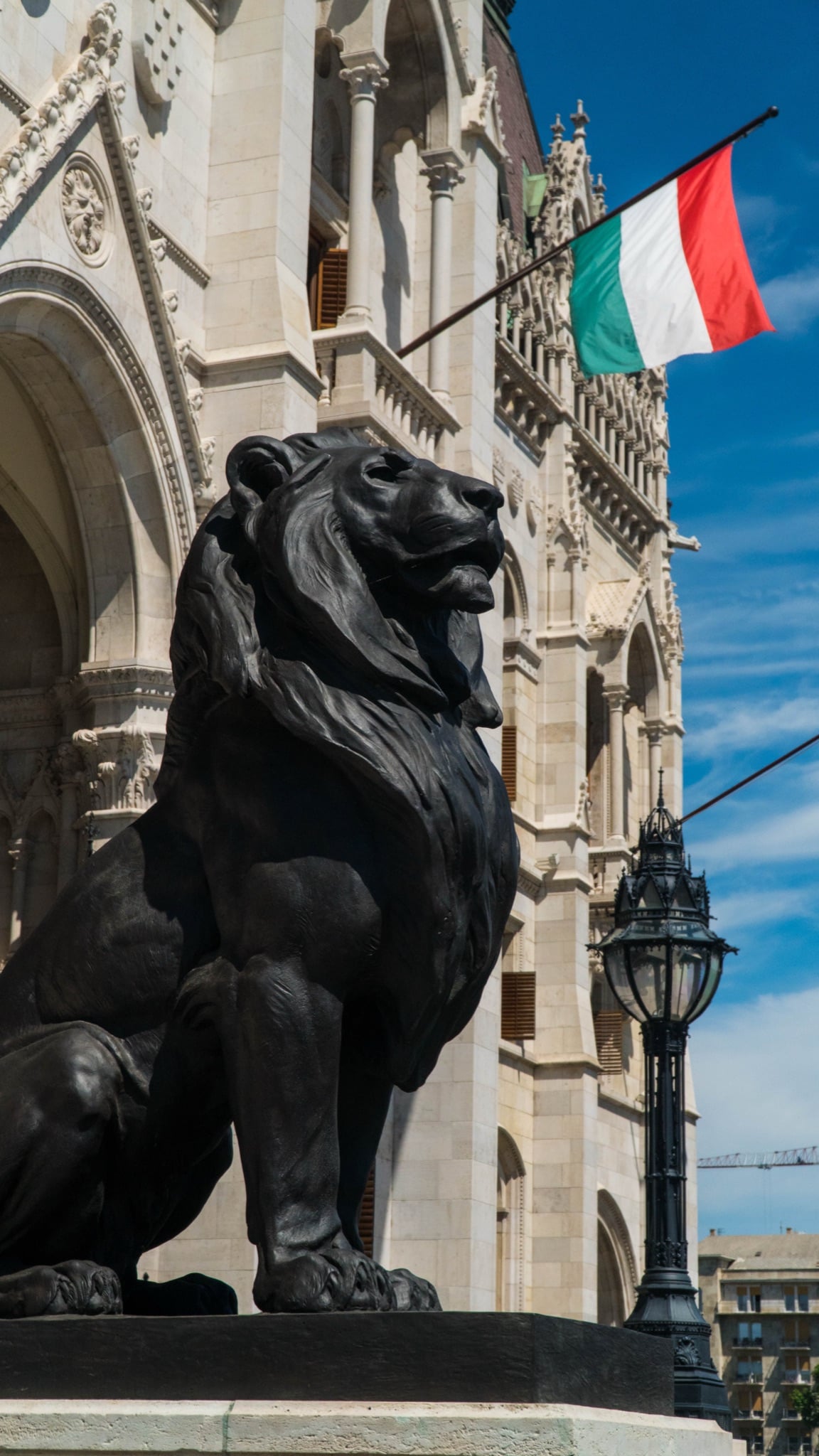 A bronze lion below the Parliament wall as the Hungarian tricolor flies overhead