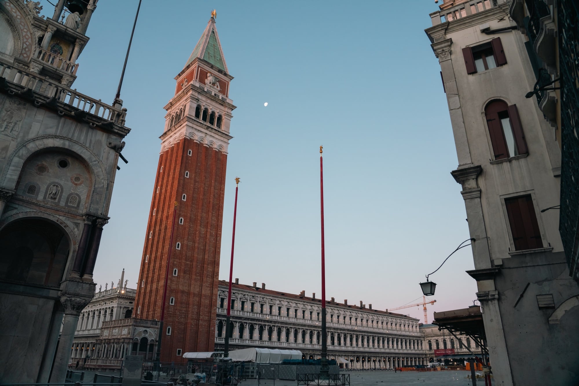Piazza San Marco at dusk, the brick Campanile with its green pyramid and golden angel above the arcaded Procuratie, a moon in the sky