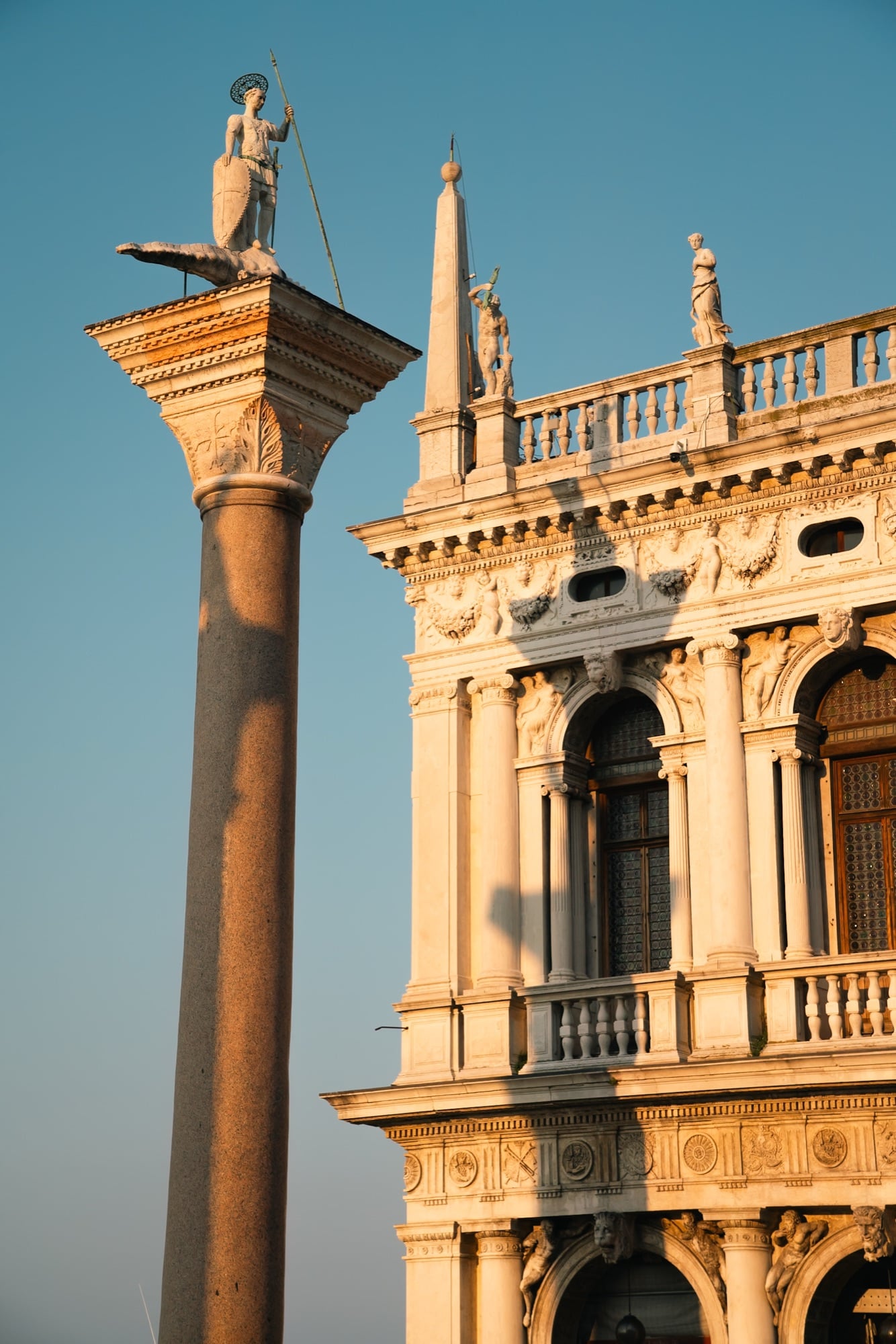 The column of Saint Theodore standing on his crocodile beside the ornately carved corner of the Biblioteca Marciana in golden light