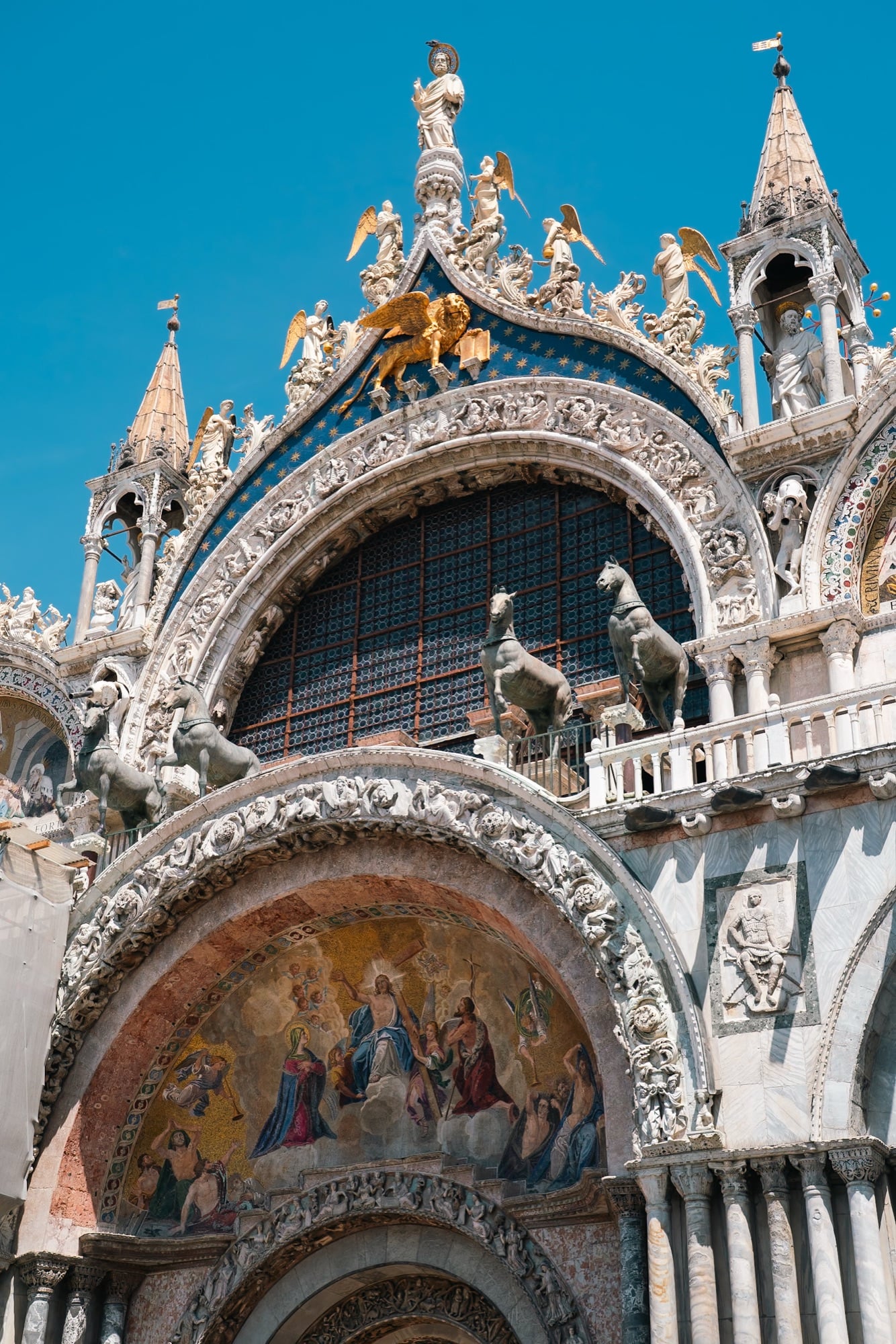 A detail of St Mark's Basilica — the four bronze horses and the golden winged lion of Saint Mark on the blue star-strewn gable against a clear sky