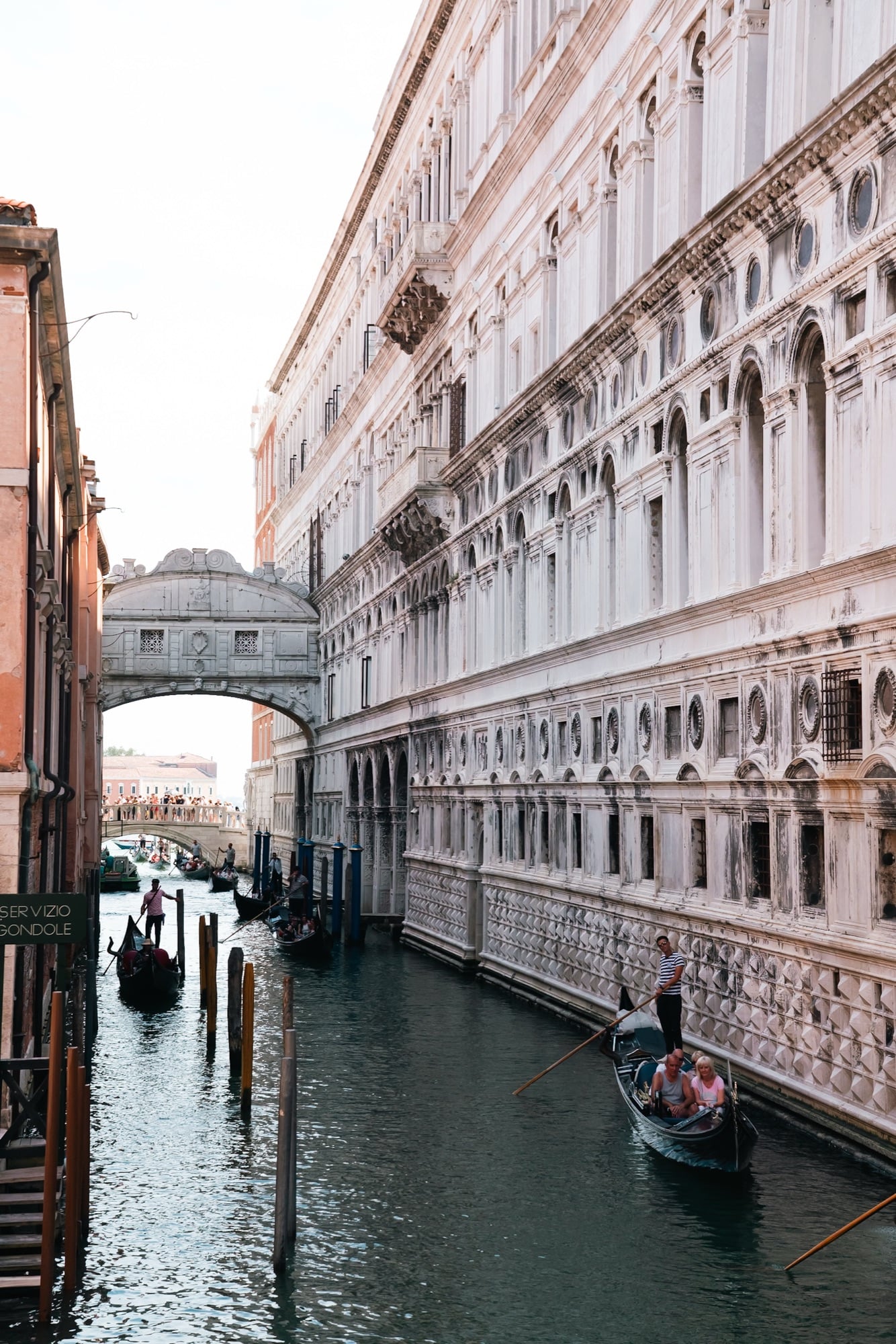 The Bridge of Sighs seen along the Rio di Palazzo beside the diamond-patterned wall of the Doge's Palace, gondolas of tourists passing below