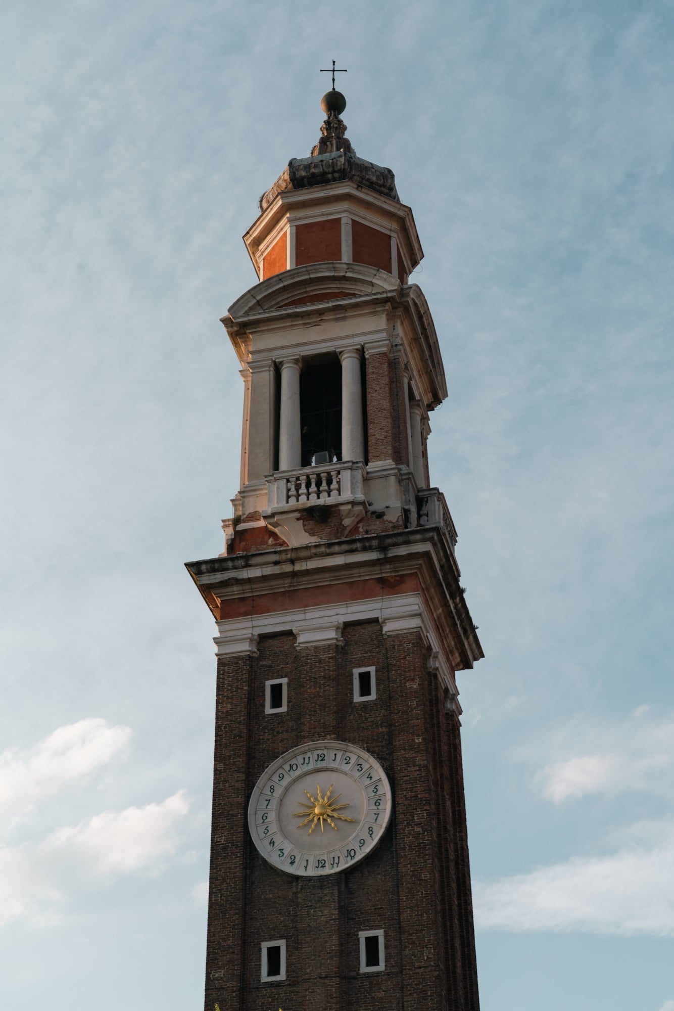 A close view of the Santi Apostoli campanile, its brick shaft crowned by a columned belfry, onion-domed lantern and gold sun clock