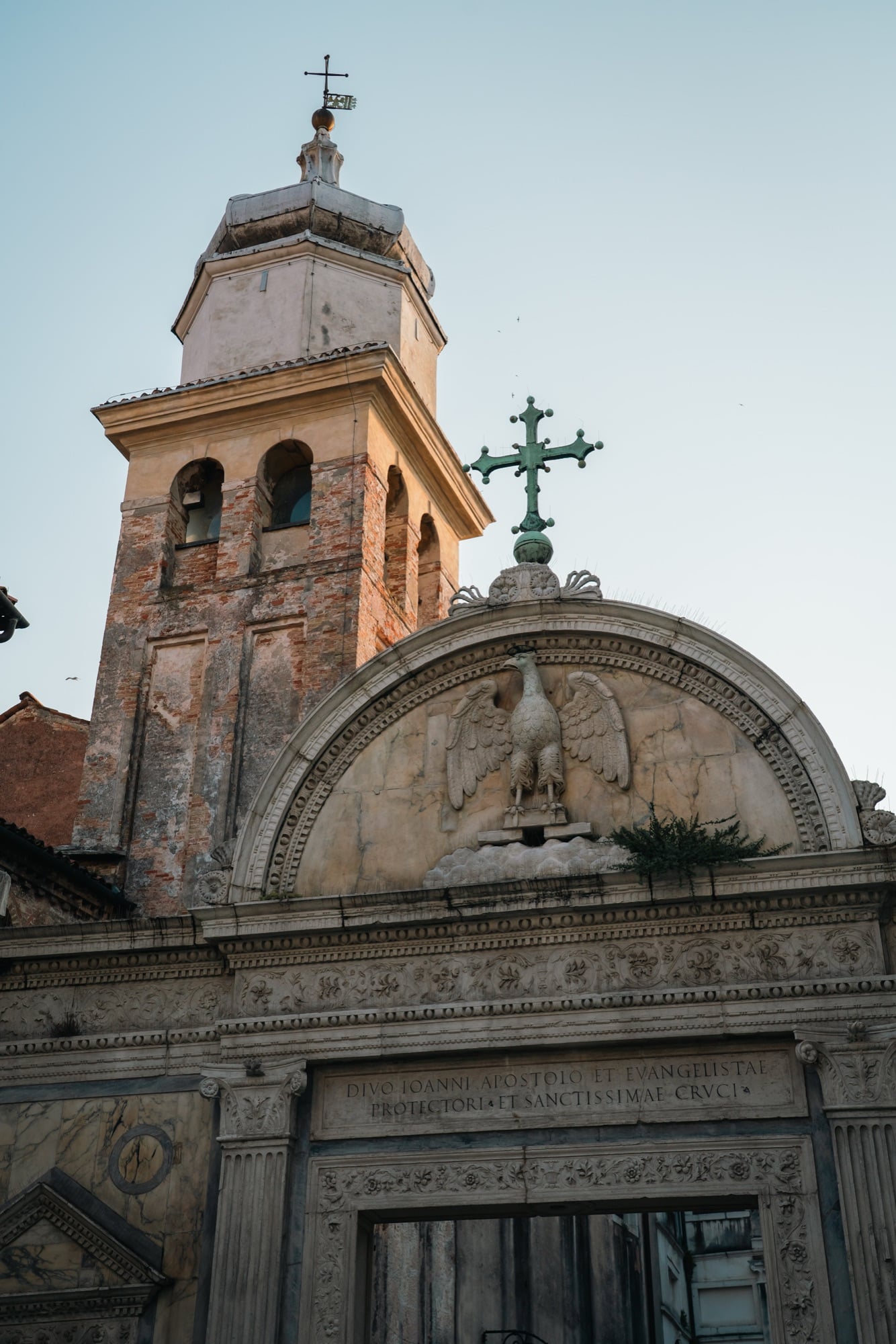 The marble portal of the Scuola Grande di San Giovanni Evangelista, an eagle relief above the arch and a leaning brick campanile behind at golden hour