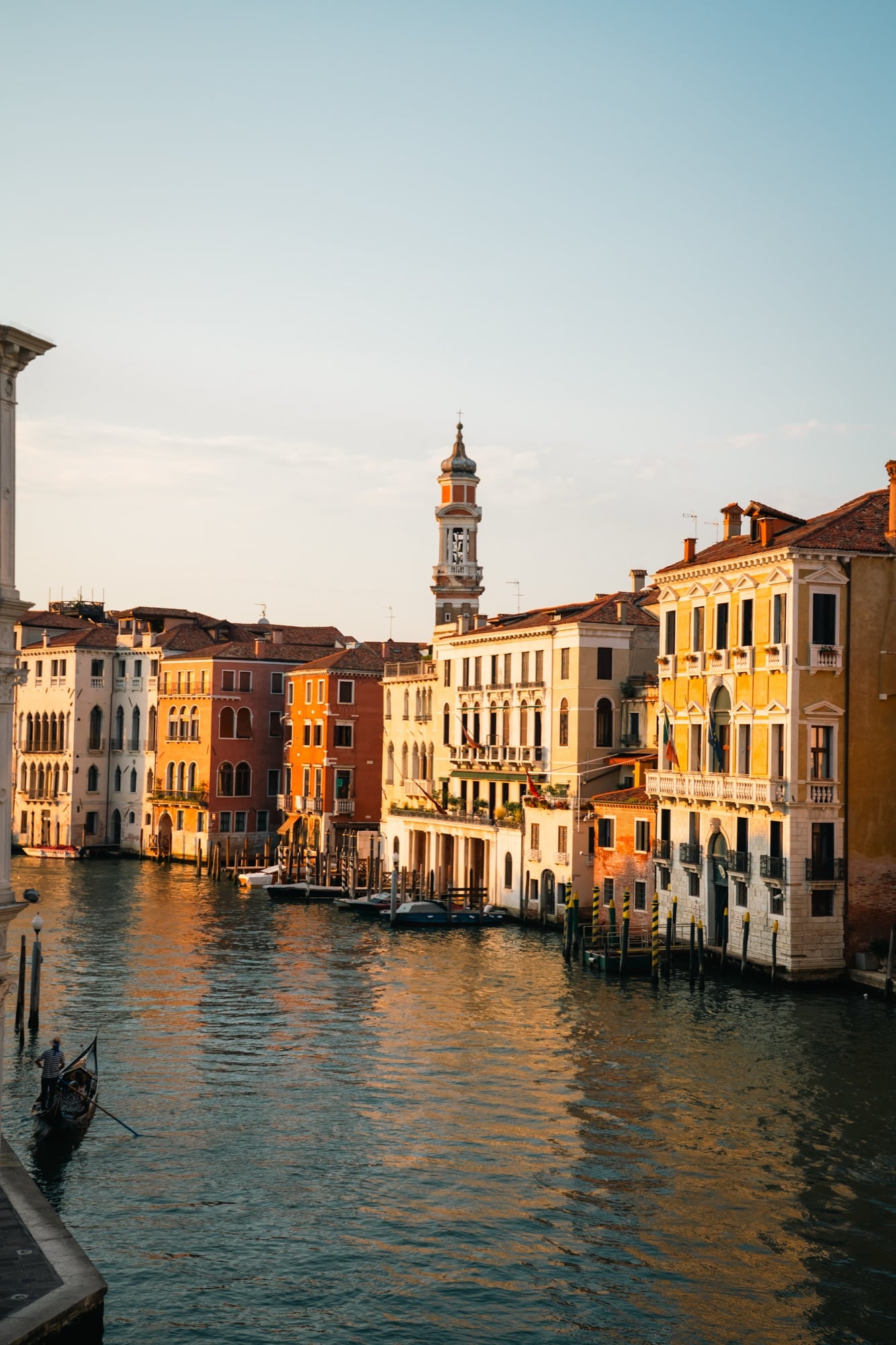 The Grand Canal at golden hour with the onion-topped campanile of Santi Apostoli in the distance and a gondolier at lower left