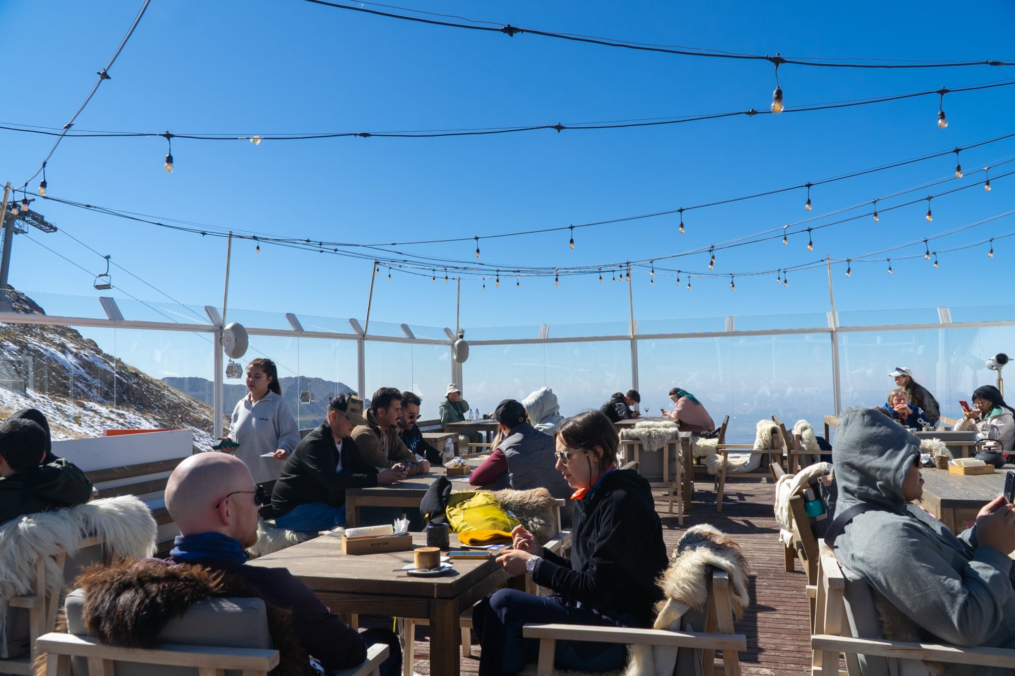 An open-air terrace café strung with lights and draped in sheepskins at the top of Shymbulak