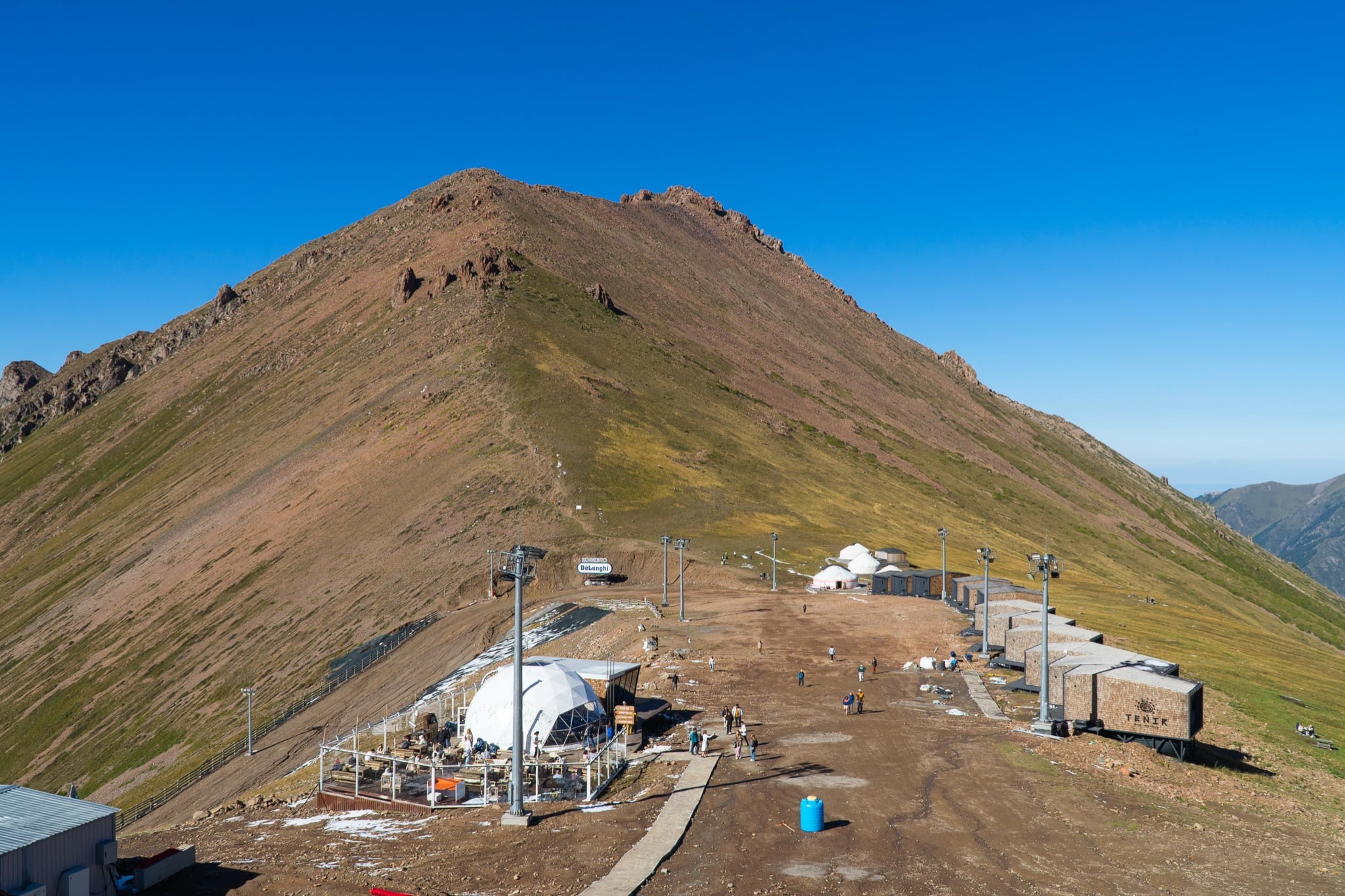 A pyramid peak rising above the Shymbulak upper station, with yurts and chairlift towers along the ridge