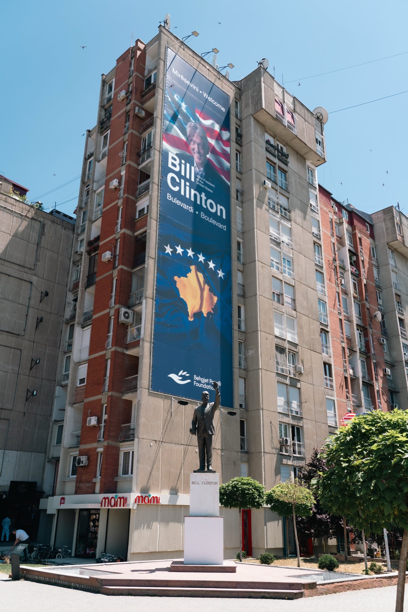 The Bill Clinton statue with arm raised on Bill Clinton Boulevard in Pristina, a huge portrait banner and Kosovo map on the building behind