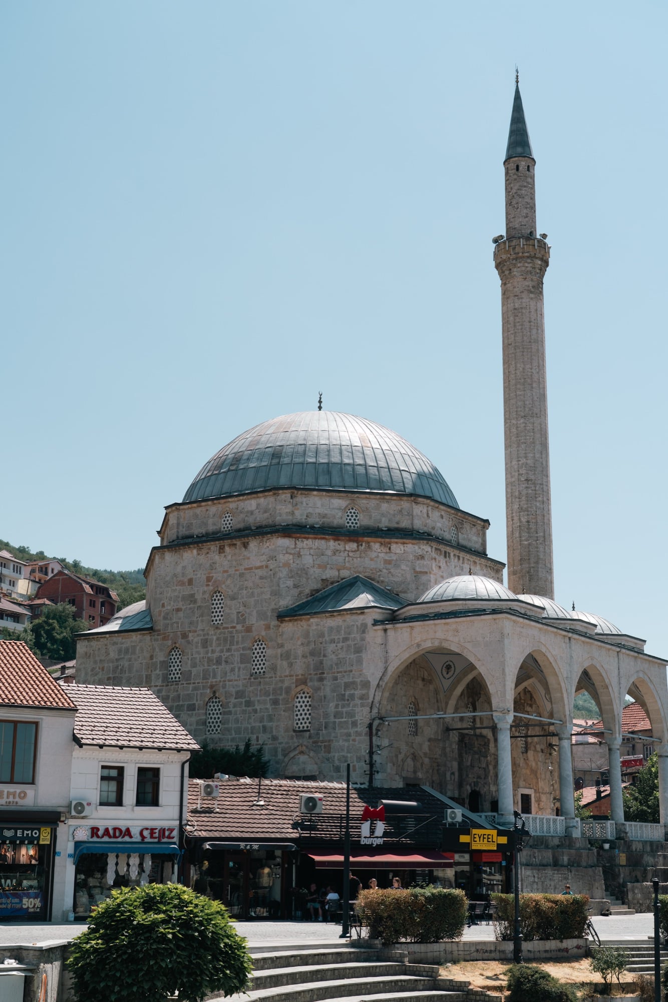 The great dome and slender stone minaret of the Sinan Pasha Mosque towering over the shops and square of central Prizren