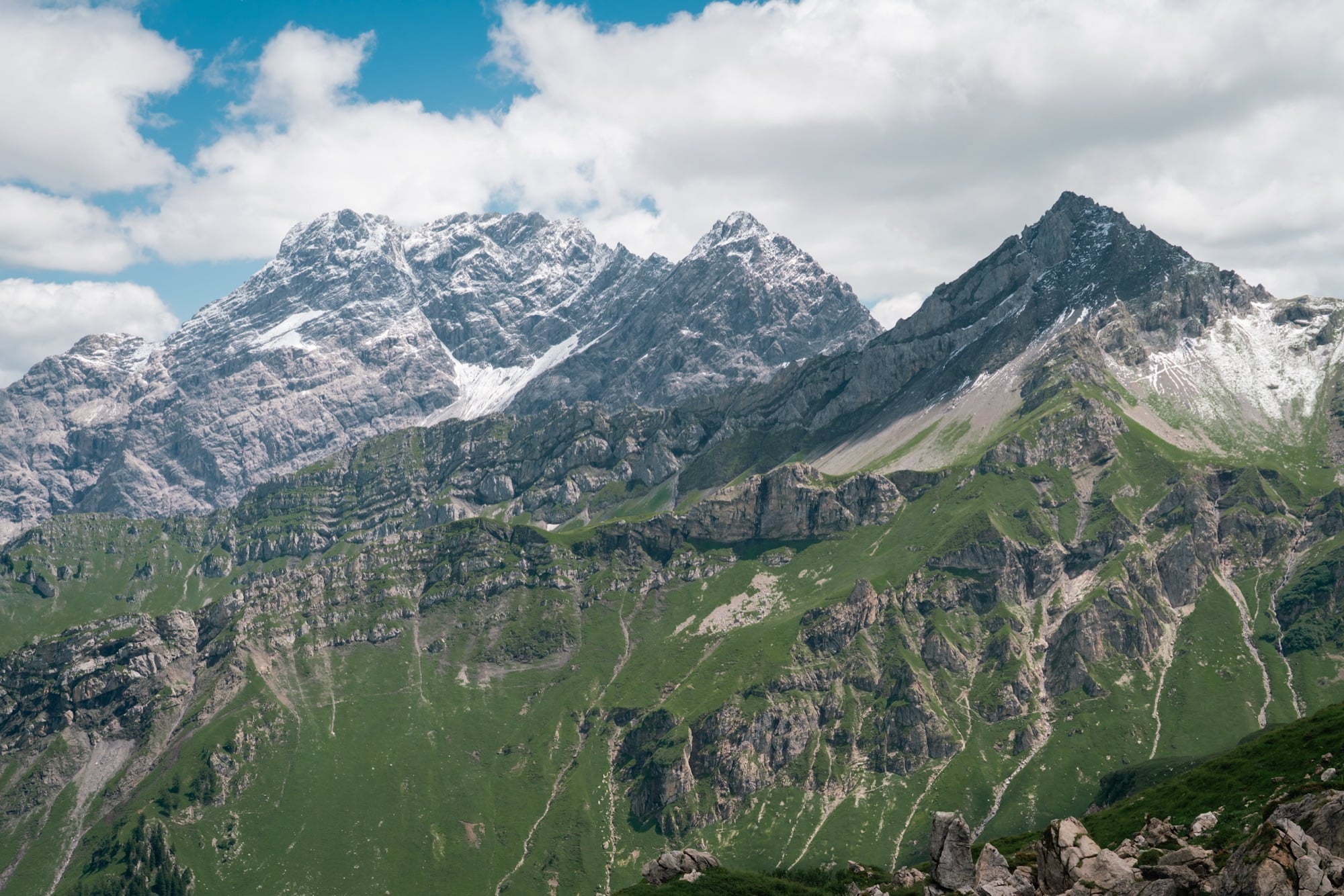 The snow-streaked wall of the Rätikon massif rising above green lower slopes under a blue sky