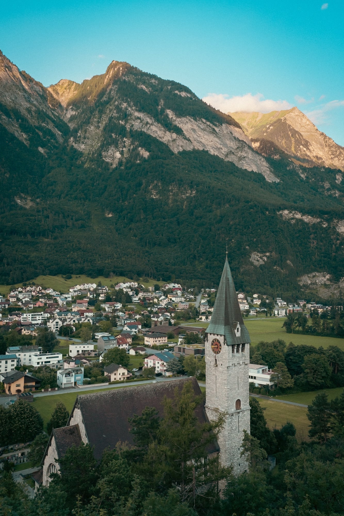 The tower of St. Nicholas church rising over Balzers, the great wall of the Rätikon glowing behind at dusk