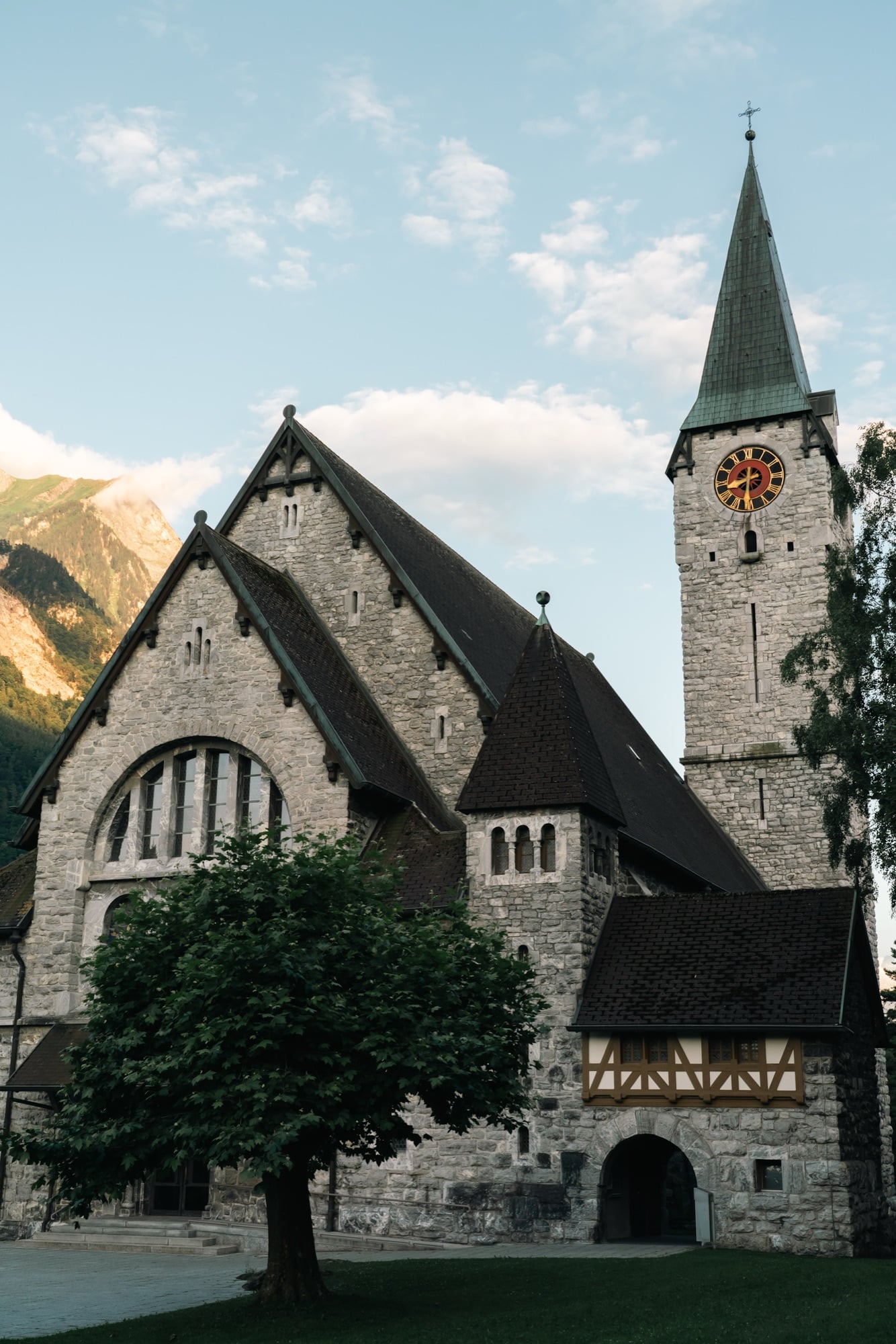 The grey-stone parish Church of St. Nicholas in Balzers, its tall copper-spired tower and red-gold clock catching the last light