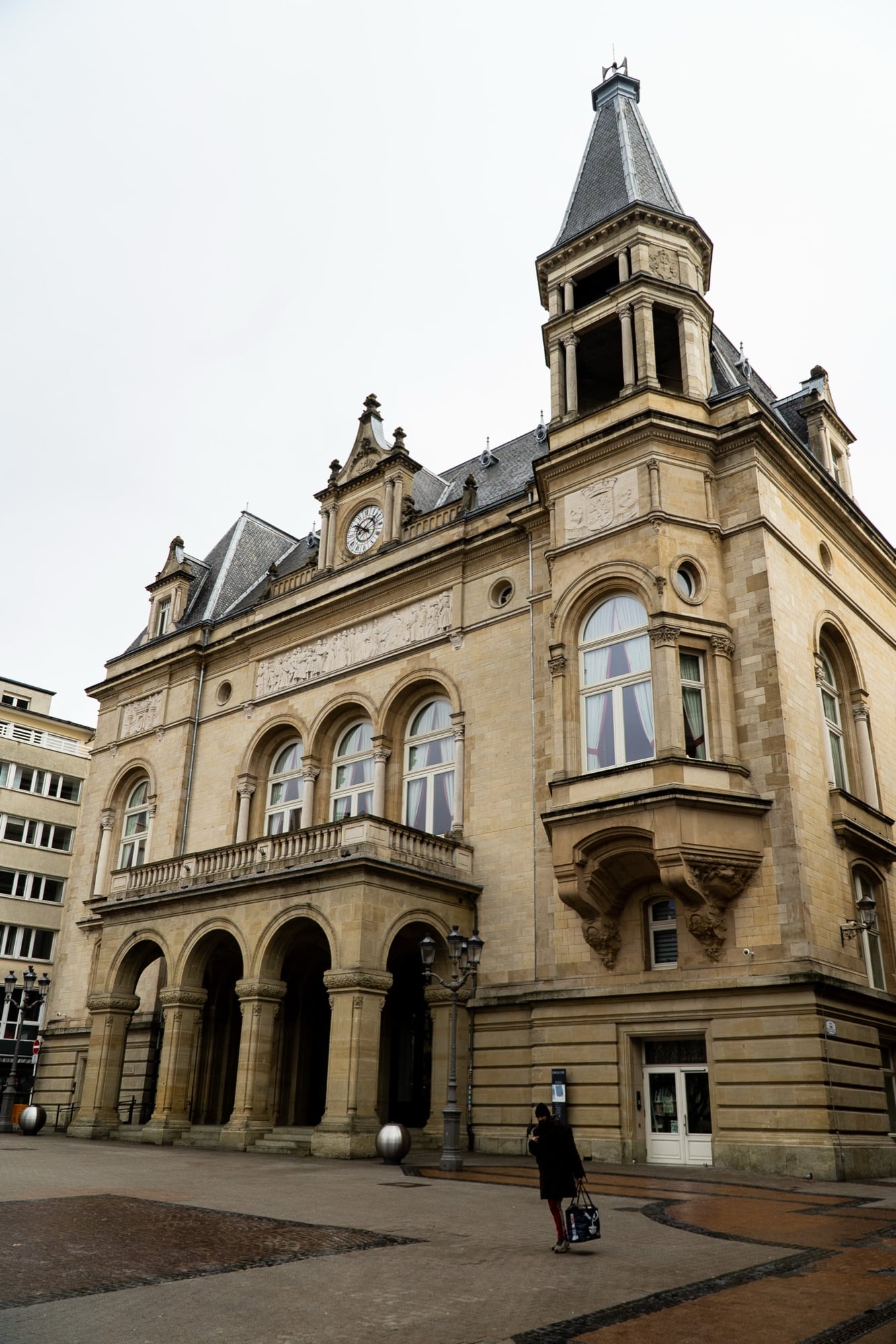A grand civic building with a corner belfry and arcaded portico rising over the square, Luxembourg City