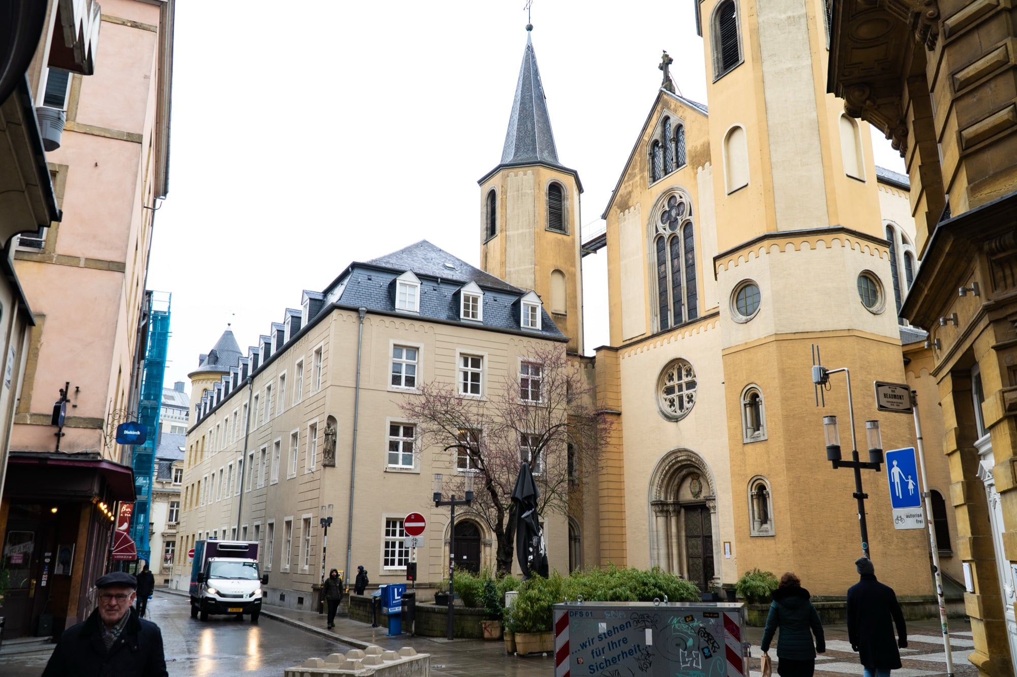 A yellow-stone church with a slate spire on a street corner in the Luxembourg City old town
