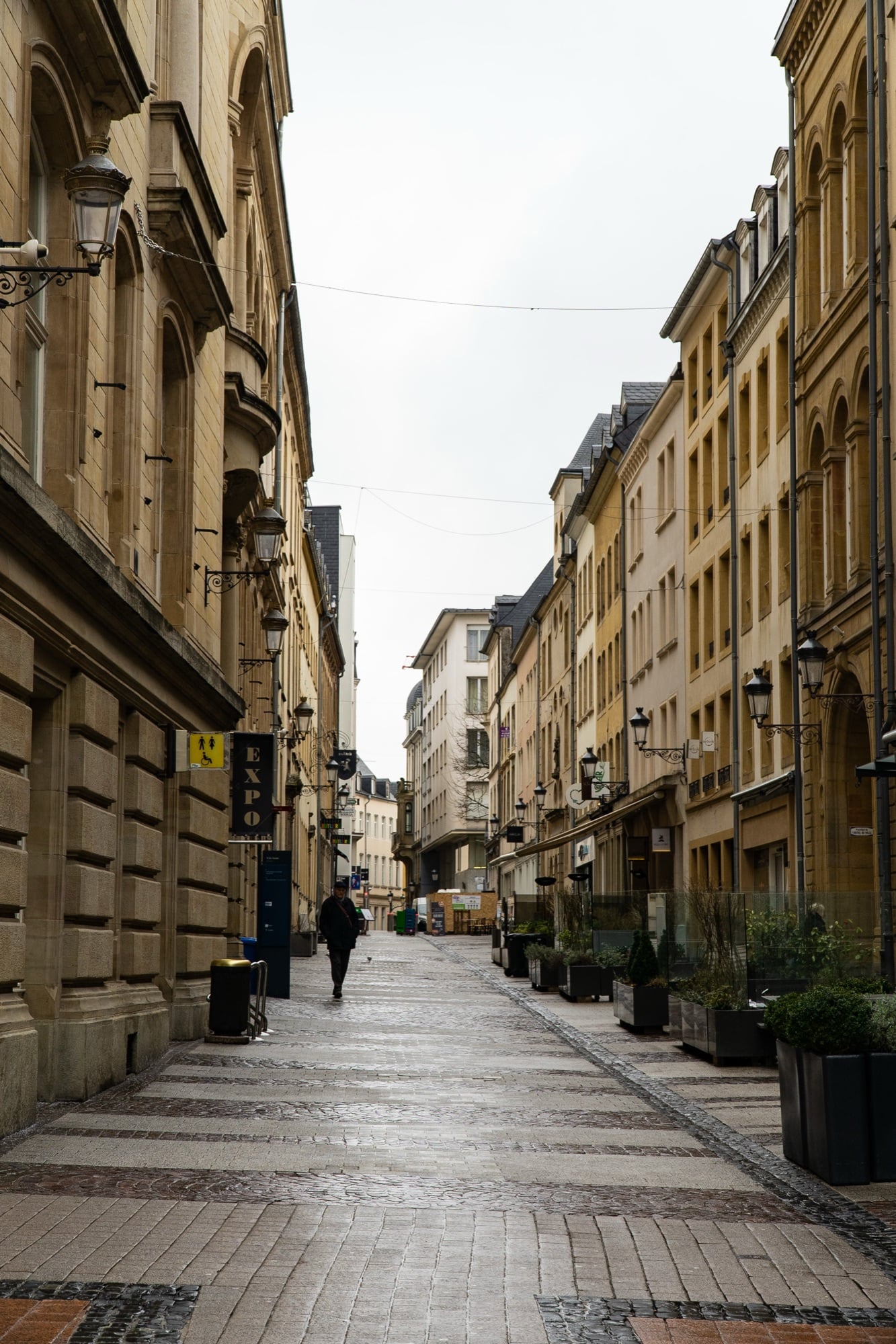 A lone figure on a quiet cobbled street lined with ornate wrought-iron lamps in the Luxembourg City old town