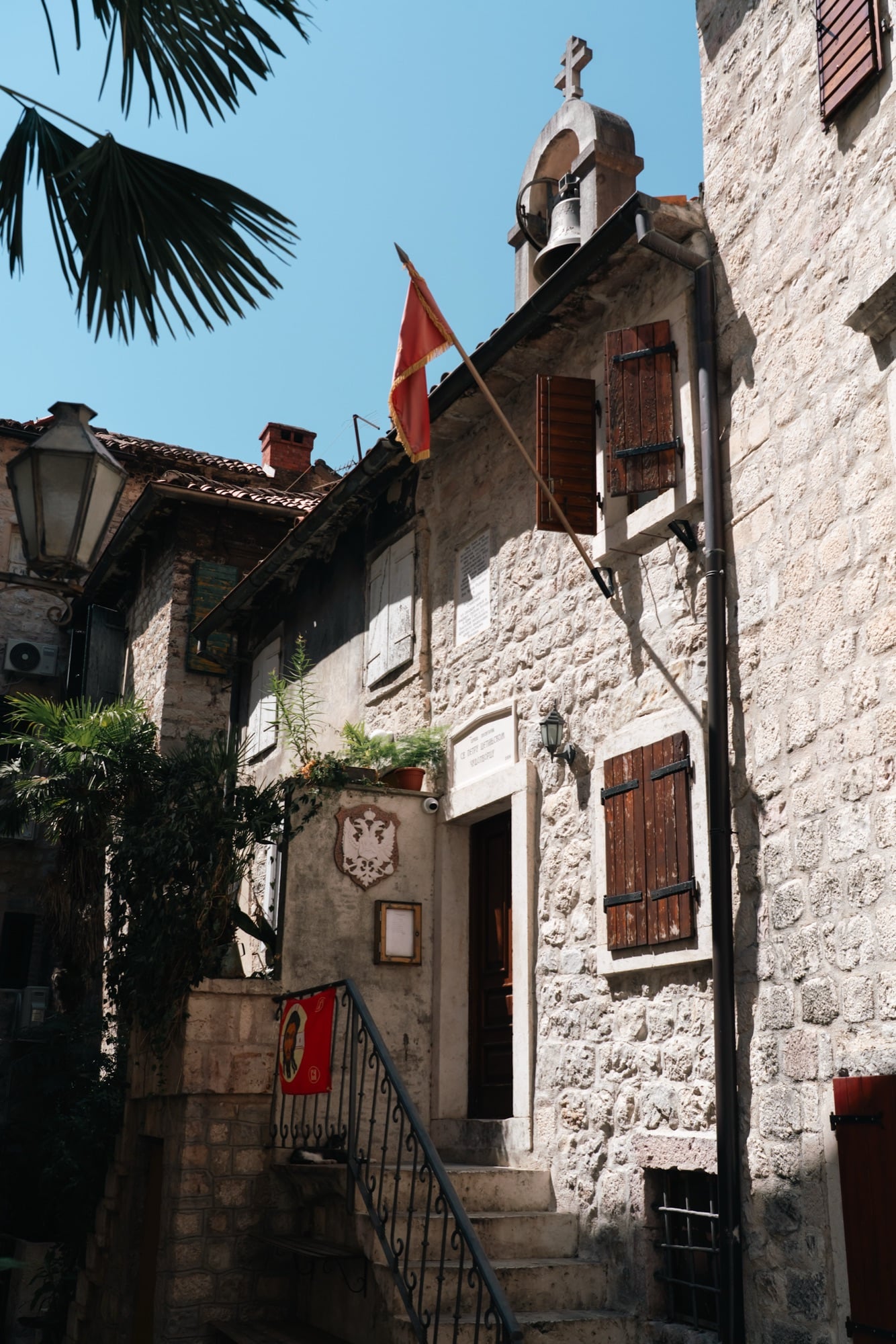 A stone stairway in Kotor's old town leading up to a small church, a Montenegrin flag and hanging bell above the doorway