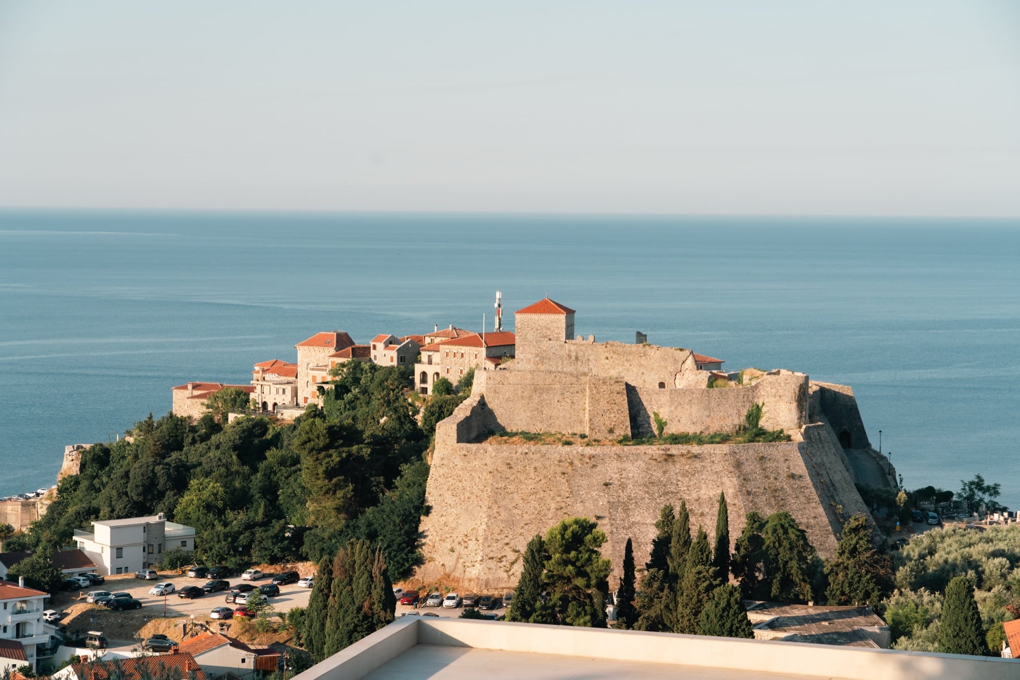 Ulcinj's old town and fortress walls crowning a headland above the calm Adriatic, the sea stretching flat to the horizon