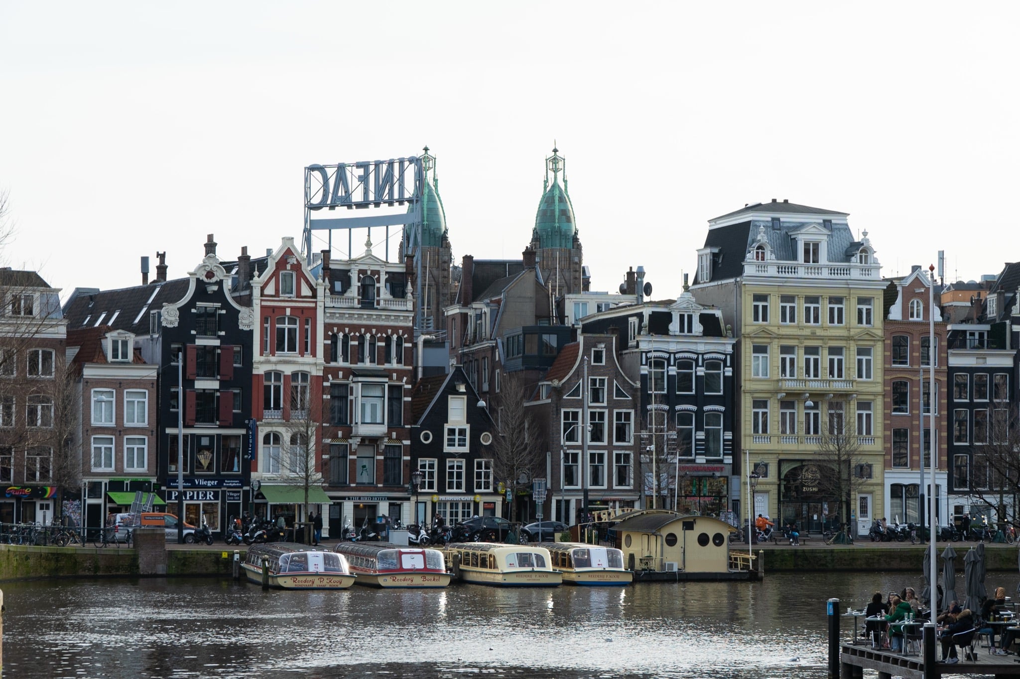 Canal-tour boats moored along the Amstel below a row of gabled waterfront houses