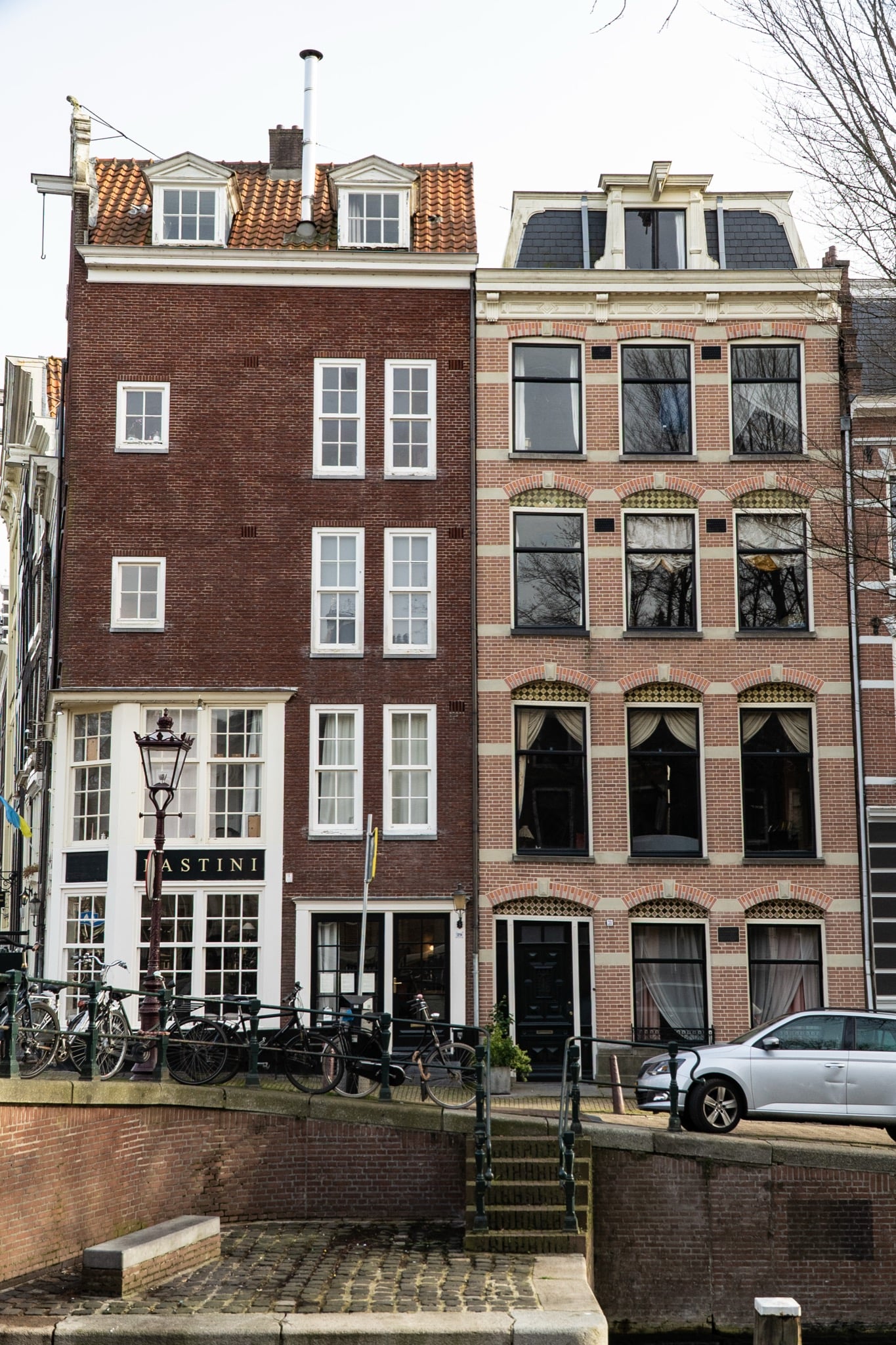 Two narrow canal houses above the Bastini shopfront, bicycles lining the bridge railing